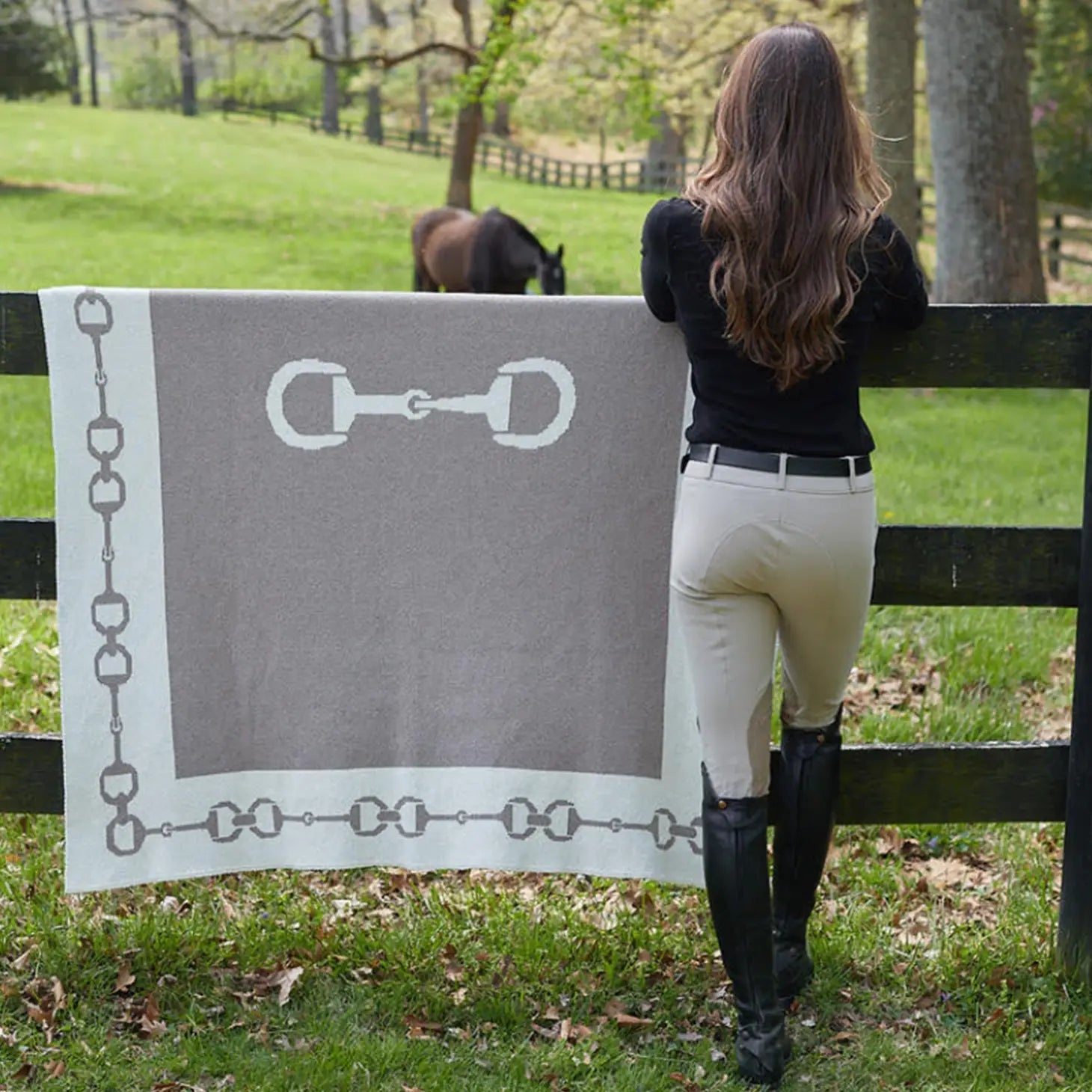 A female equestrian standing next to Equestrian Snaffle Bit Border Throw hanging on paddock fence with horse in background
