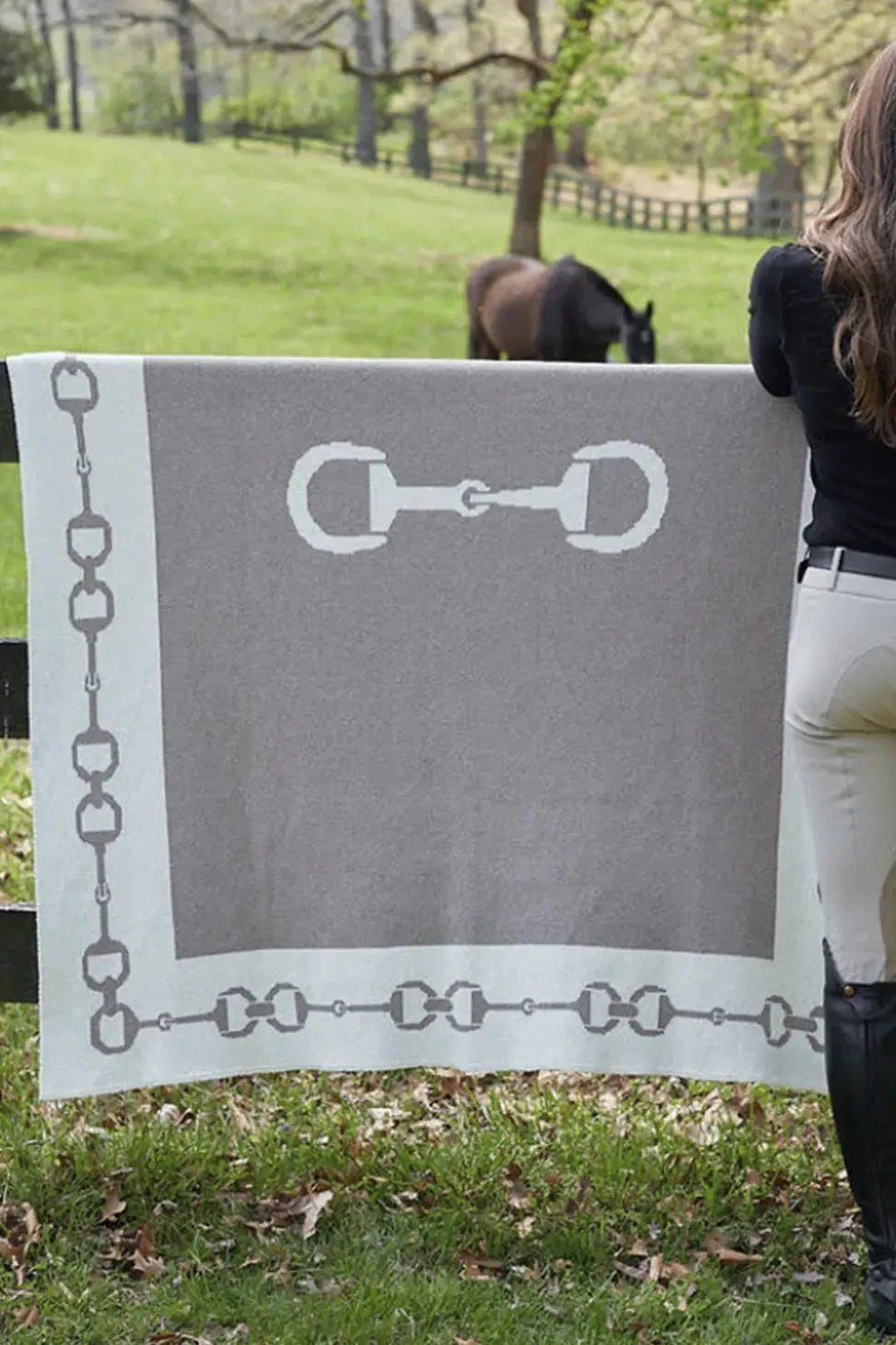 A female equestrian in formal clothing standing next to the Equestrian Snaffle Bit Border Throw hanging over a paddock fence