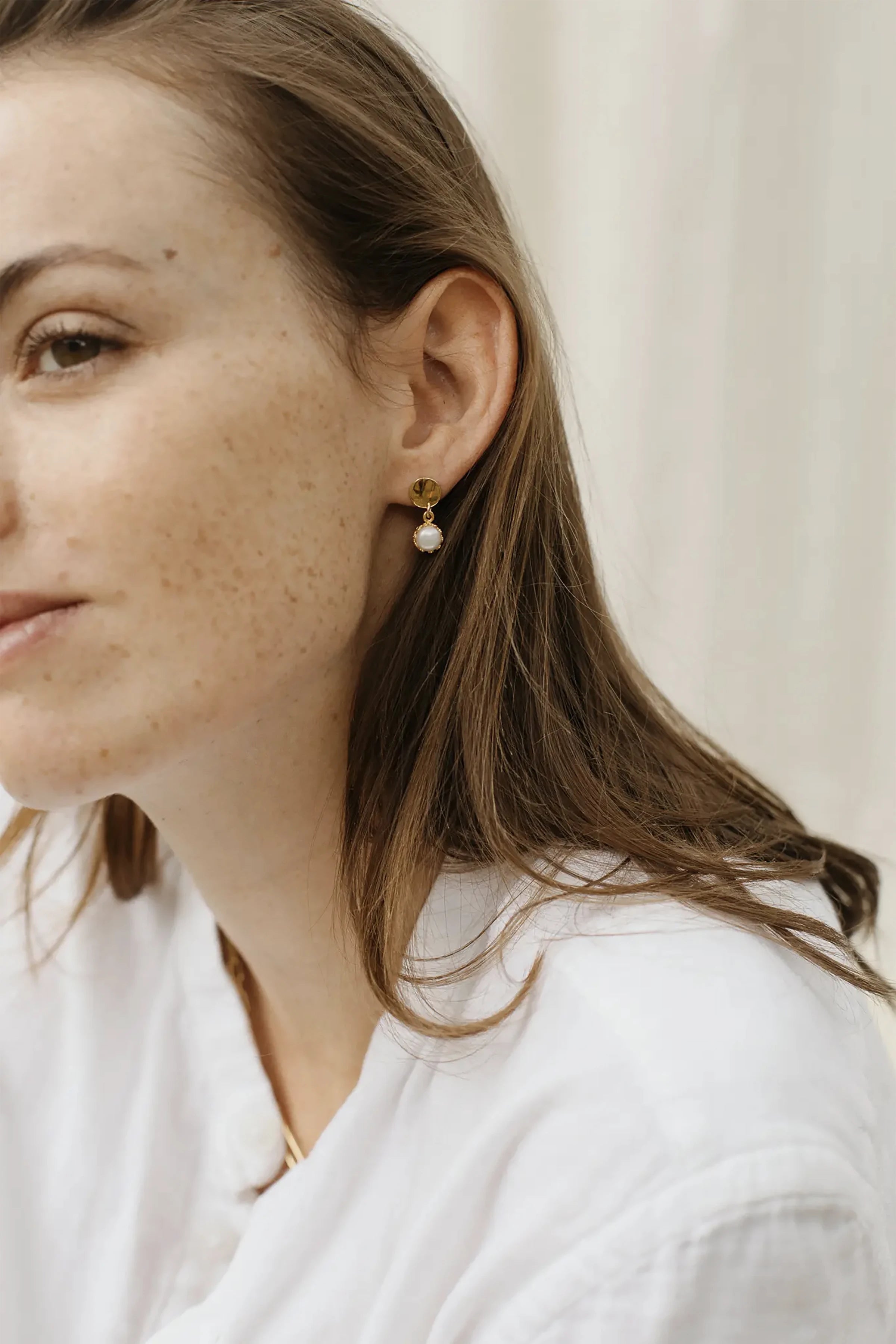 Fontaine Freshwater Pearl Gold Earrings on a model's left ear. The gold circle lays on the ear, while the pearl and bloom setting hangs below the ear.