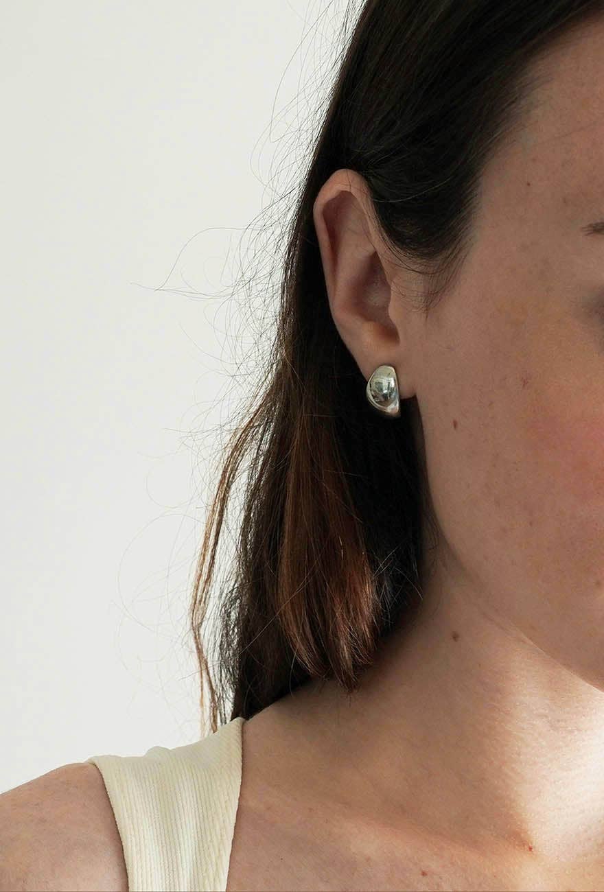Huggie Earrings Sterling Silver is worn by a model showing her right ear. The earring closely hugs the ear.