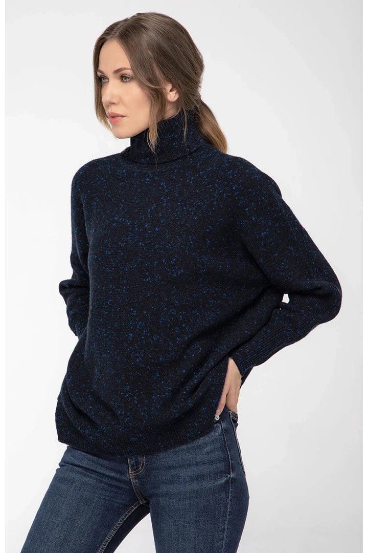 A woman wearing a ponytail is standing in front of a white background with both arms on her hips, wearing the Italian Cashmere Blend Turtleneck and blue jeans. You can see the relaxed fit.