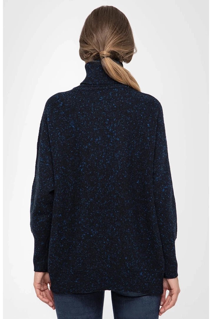 A woman wearing a ponytail is standing in front of a white background wearing the Italian Cashmere Blend Turtleneck and blue jeans. She is showing the backside of the garment. You can see the relaxed fit.