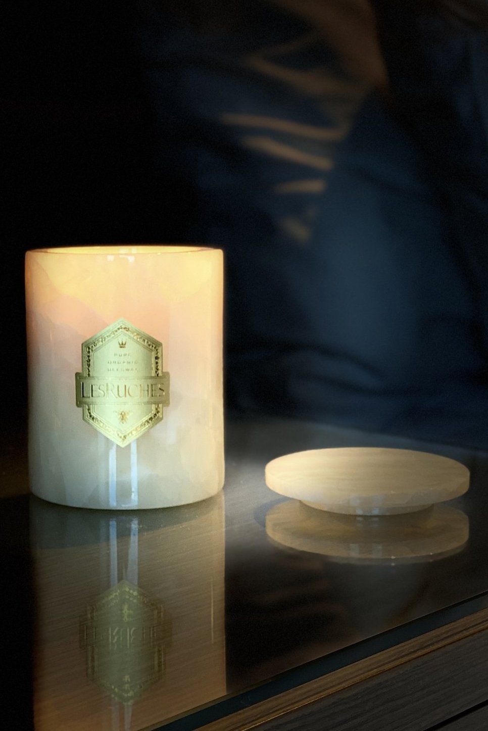 Gardenia Onyx Partfaite Beeswax Candle 8 oz and lid on table with pant leg in the background