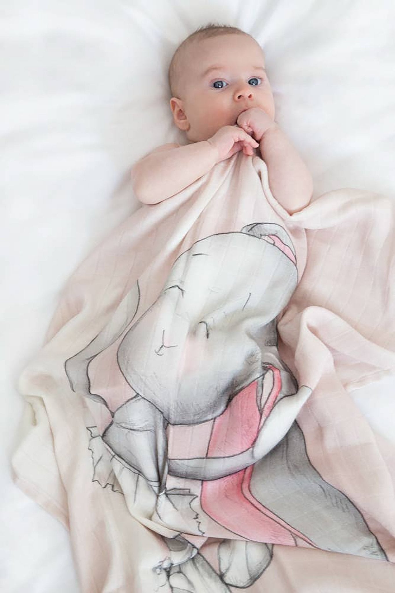 A baby is laying inside a crib staying warm underneath the Joyful Ballerina Bamboo Swaddle - L'Atelier Global