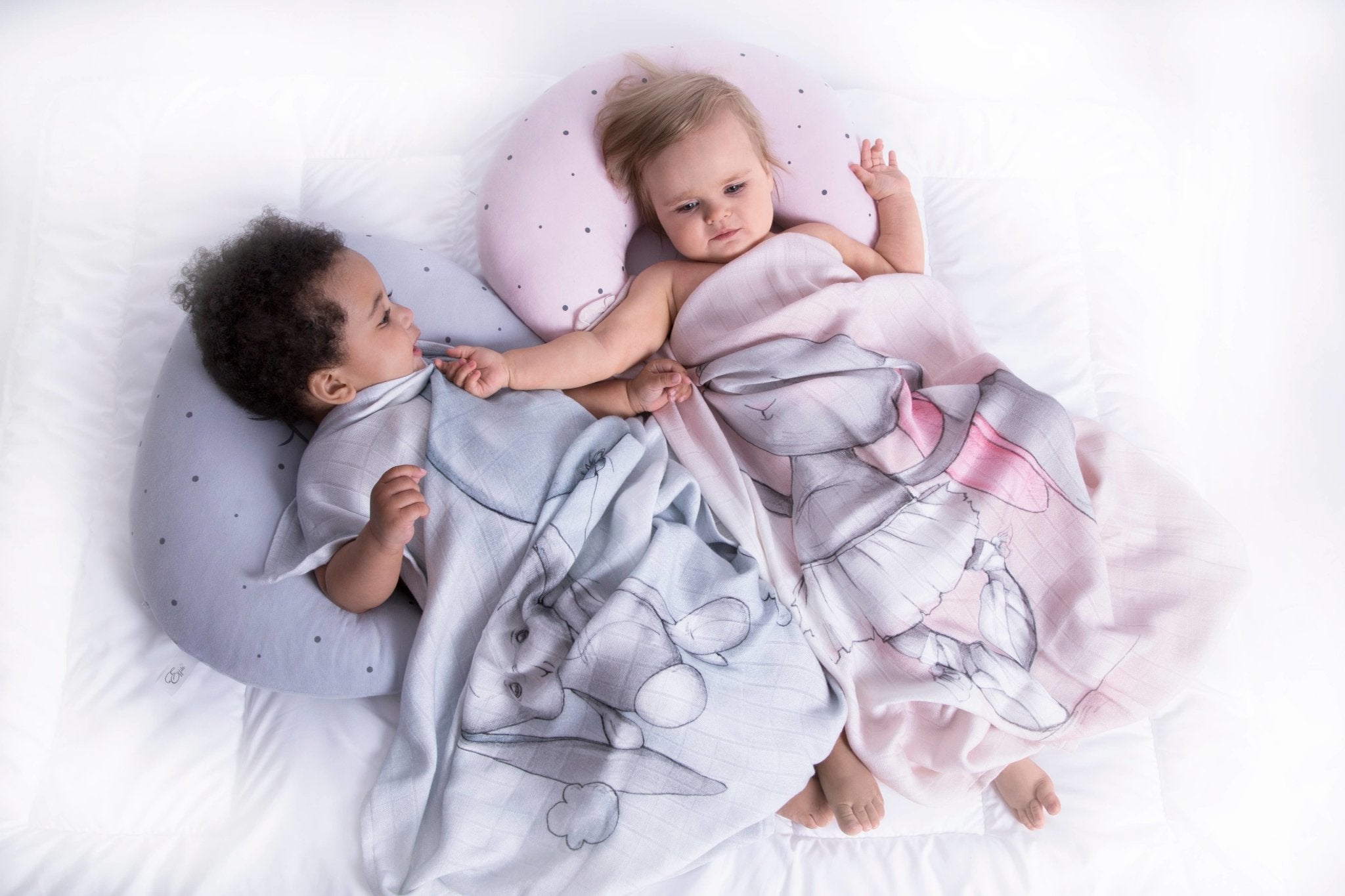 Two babies are laying inside a crib staying warm underneath the Joyful Ballerina Bamboo Swaddle - L'Atelier Global