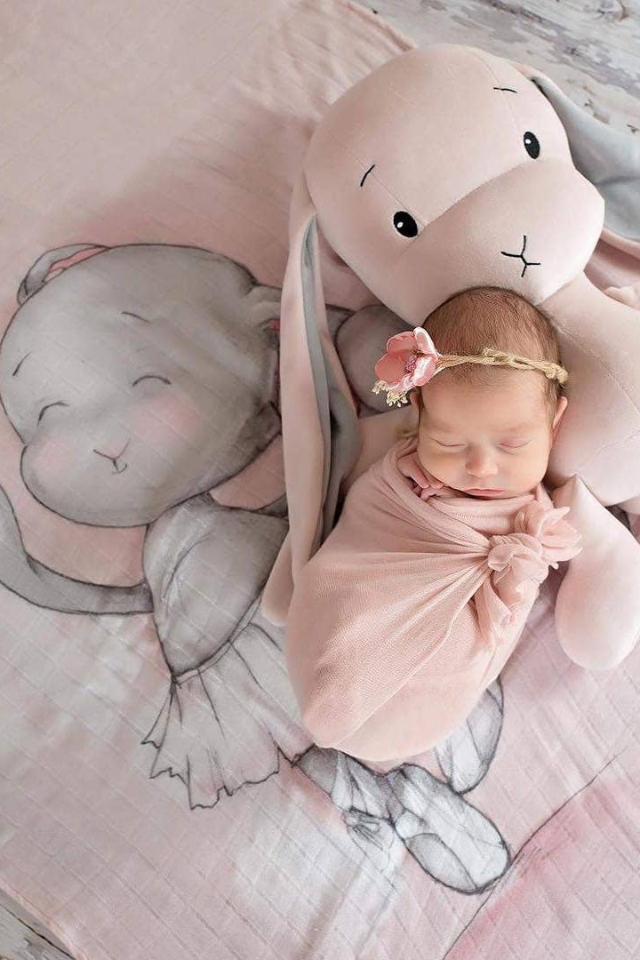 A baby is laying inside a crib staying warm underneath the Joyful Ballerina Bamboo Swaddle - L'Atelier Global