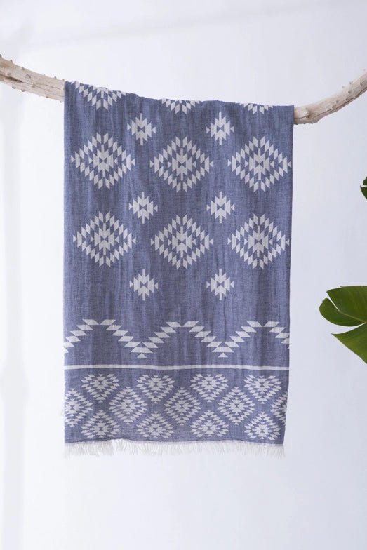 Kilim Motif Turkish Cotton Towel in dark blue and white with white fringe hanging over a tree limb in a studio