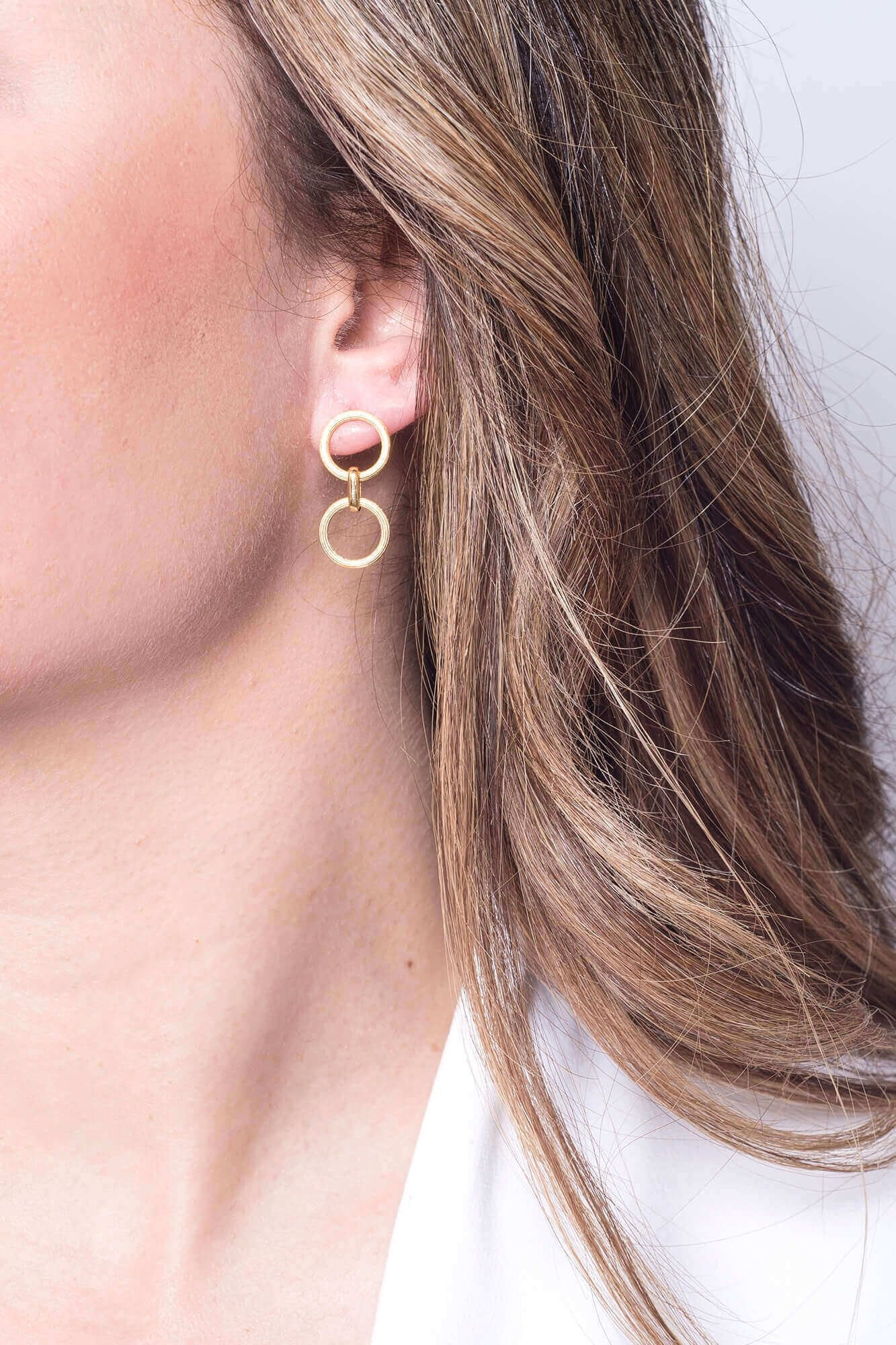 Larissa Circular Gold Dangle Earrings on a female model with lomg light brown hair showing her right ear.