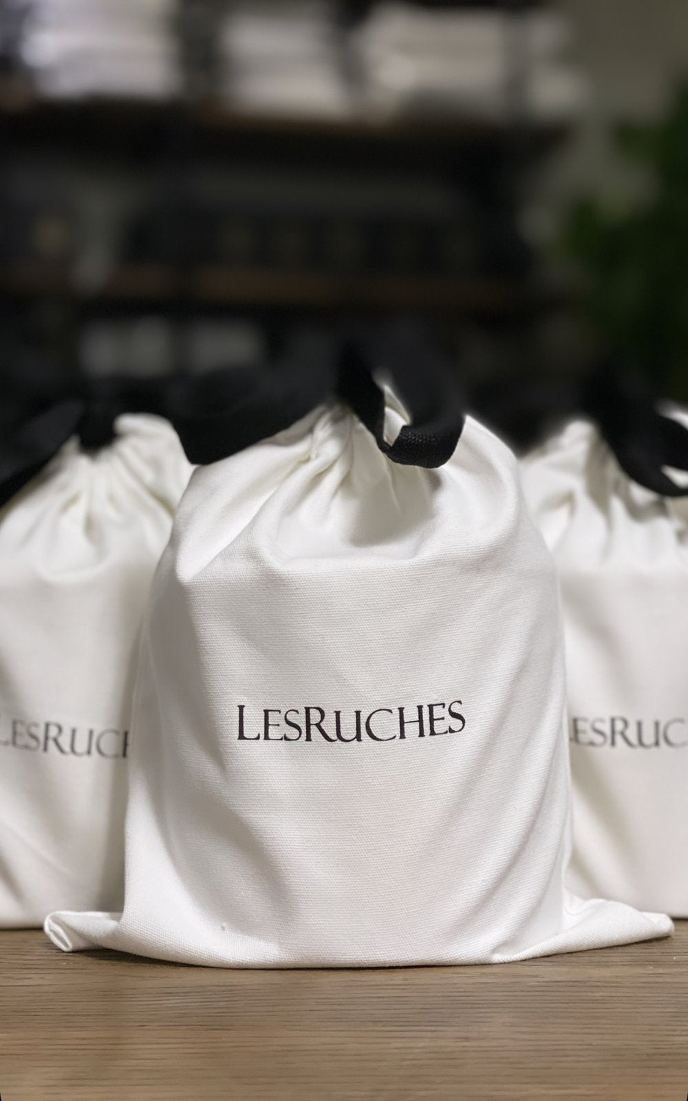 Les Ruches white silky Candle gift bags with black tie bows on a wooden table