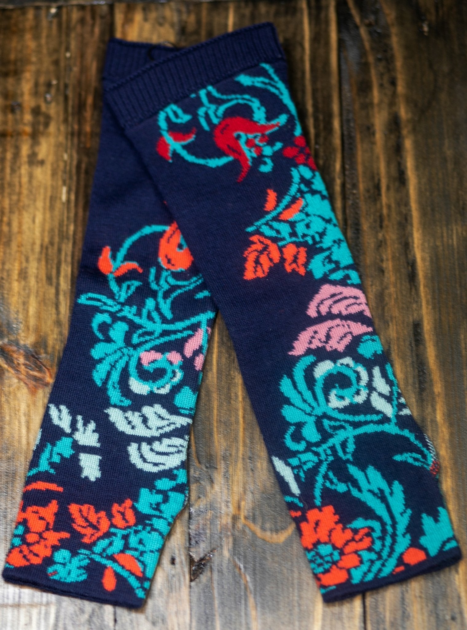 Lily of The Valley Serbian Fingerless Gloves in Blue laying crossed over each other on a wood background