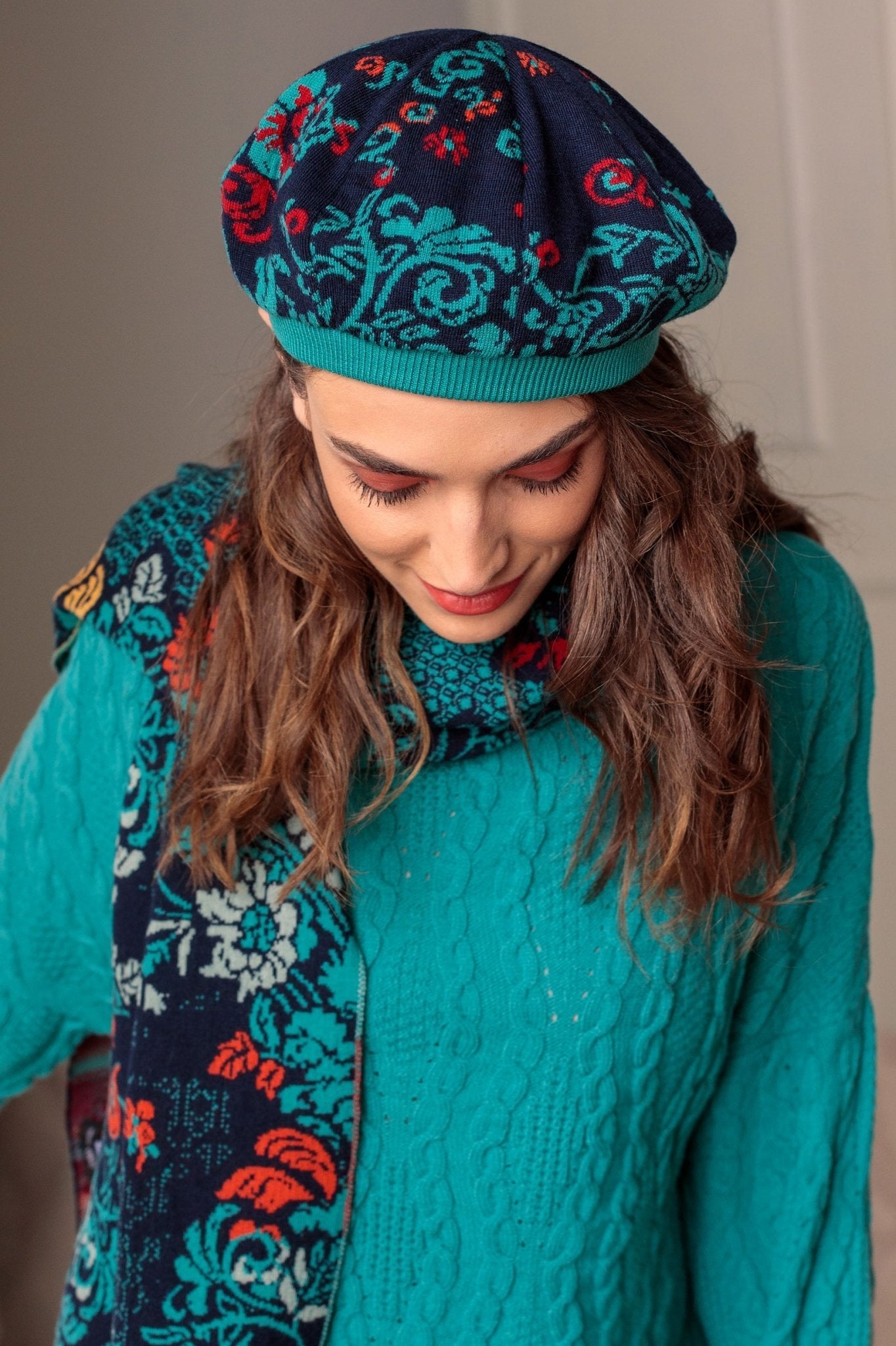 A woman is wearing the hat and scarf in blue and is looking at the floor to show the top of beret