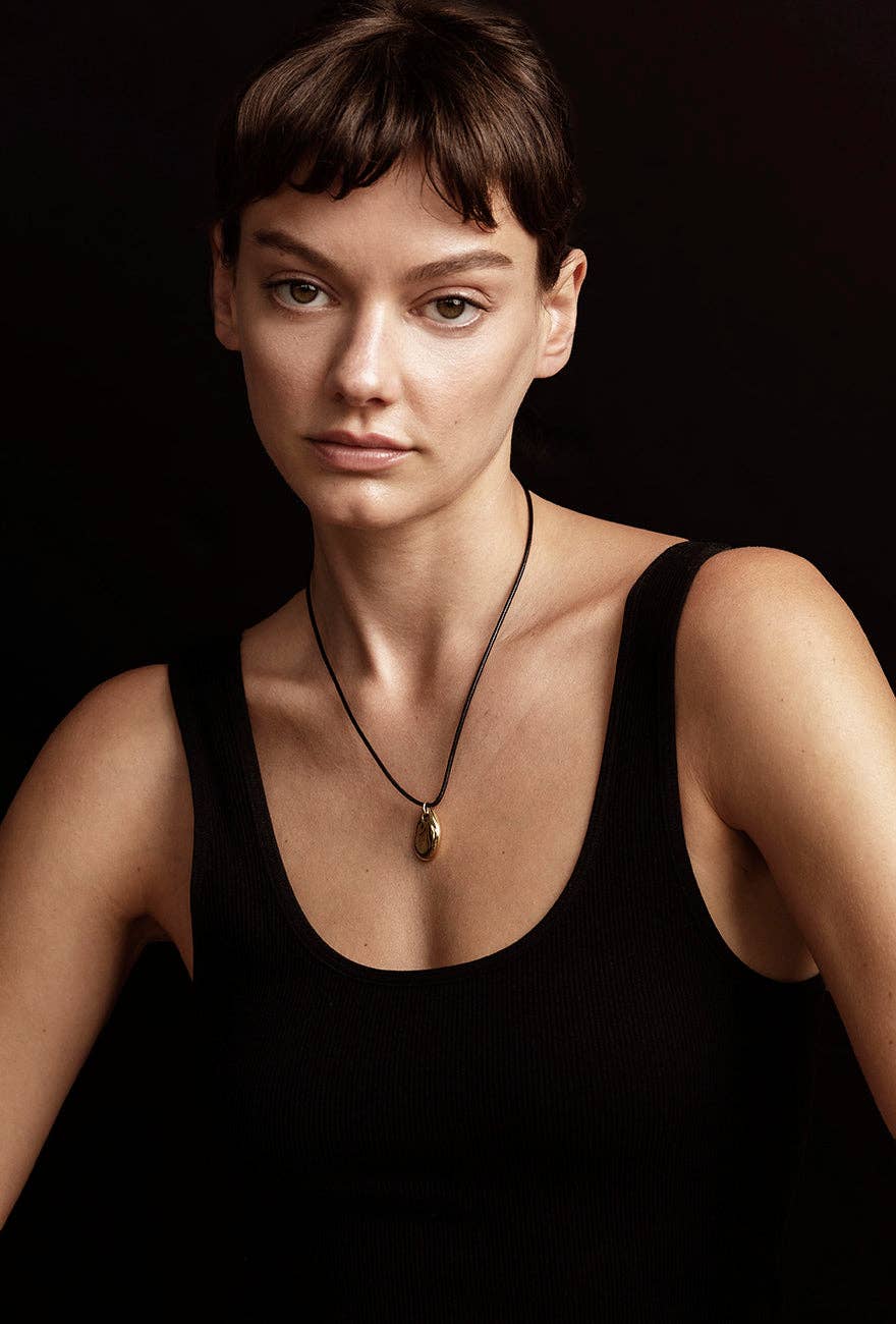 Louisa Gold Pebble Pendant Cork Necklace is worn by a model wearing a black crew shirt