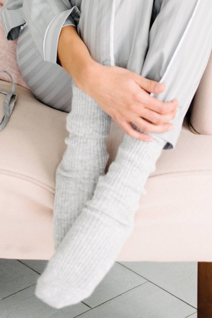 A model sitting on a white couch wearing the Luxe Cashmere Gray Sleep Sock n gray - L'Atelier Global