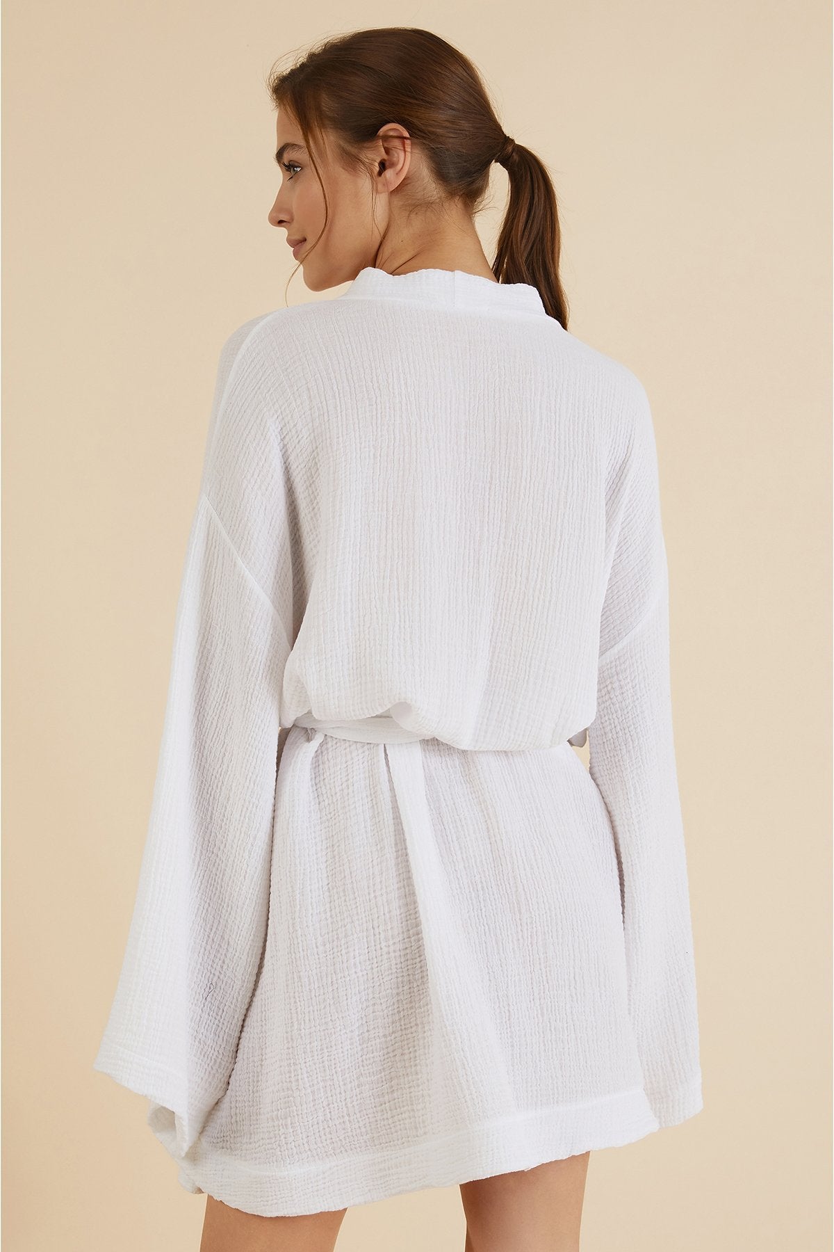 Back view of Luxe Luna Kimono Wrap on a model in front of a natural-hued background with light. She is presenting the back of the robe.