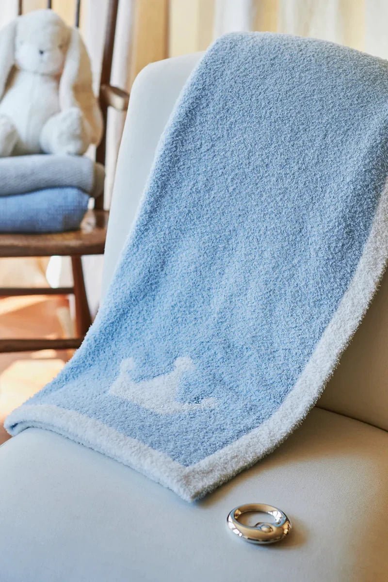 Luxe Reversible Crown Baby Blanket on blue side on the side of a crib - L'Atelier Global