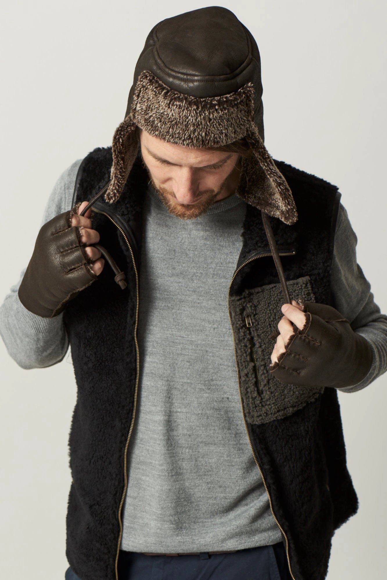 McGrath Sheepskin Storm Flap Hat in Dark Brown on a male model with a black vest and gloves- L'Atelier Global
