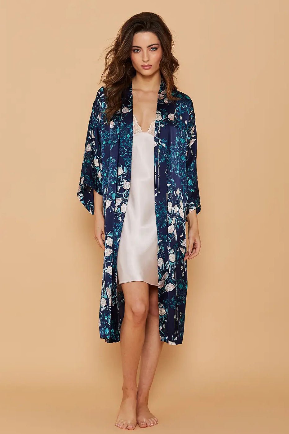 A woman is standing in front of a light gold background wearing the Midnight Garden Silk Kimono Robe opened showing an ivory silk nightgown beneath