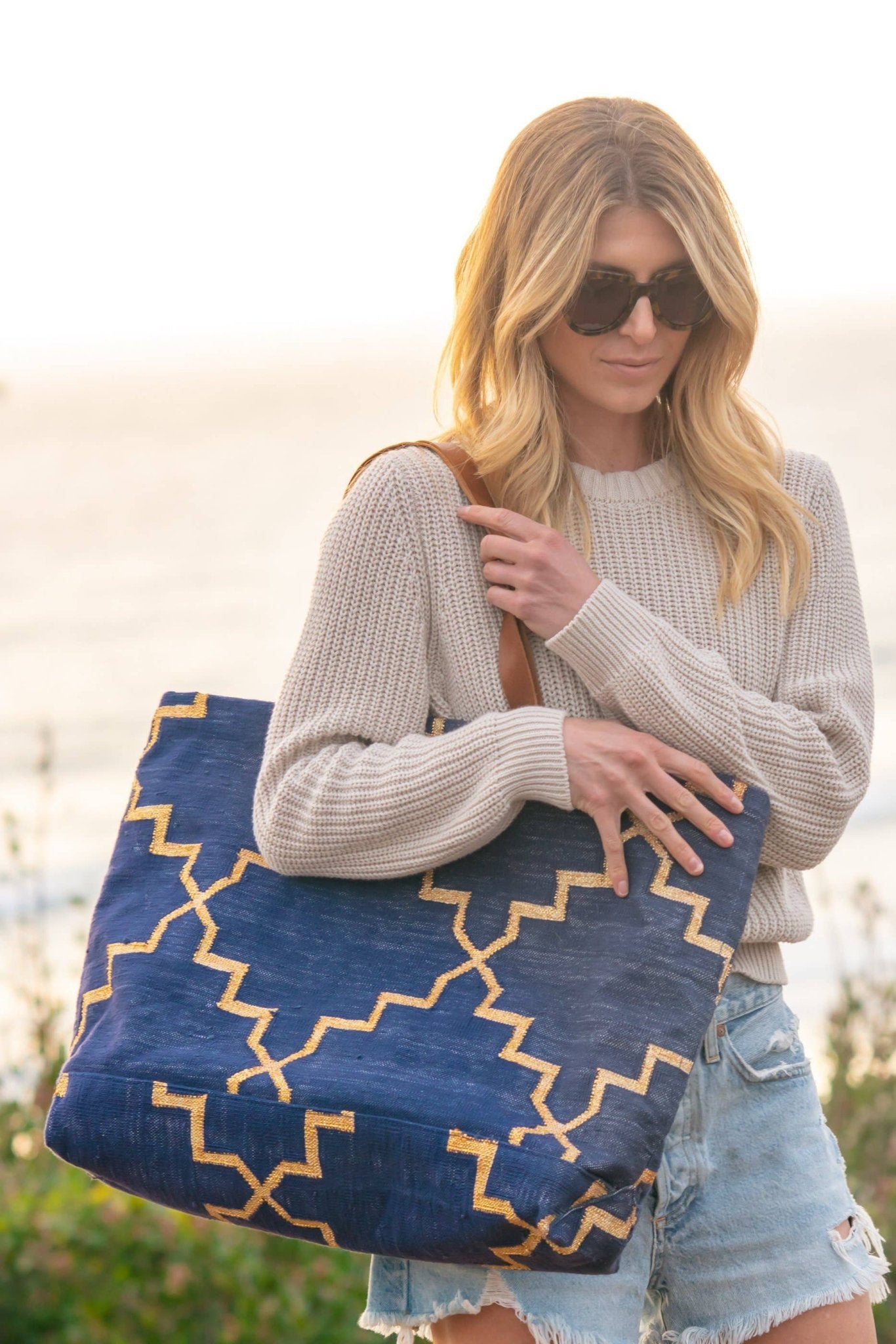 Model wearing a white sweatshirt and sunglasses carrying the Napa Get Away Tote in navy with gold accents -