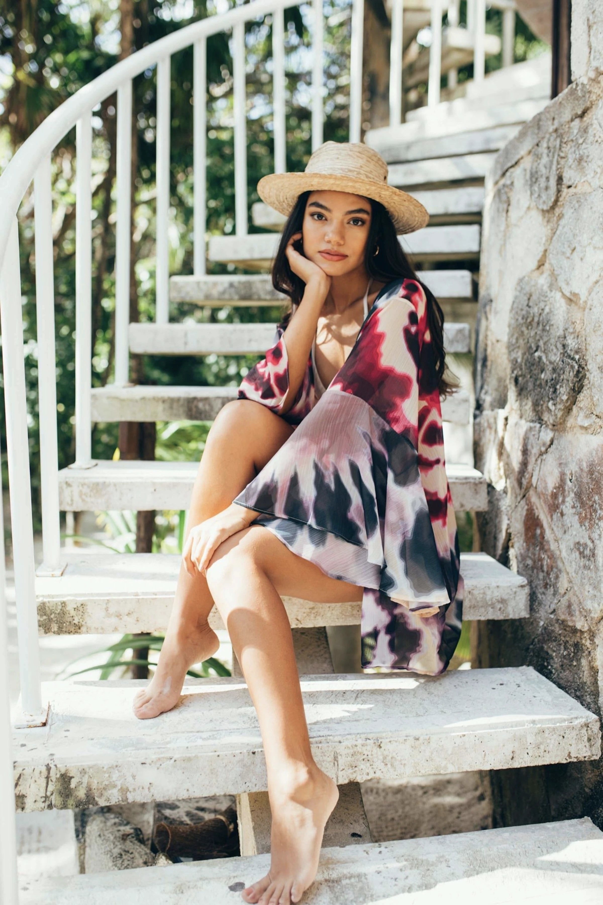 Nomad Kimono in Tie-Dye on female model wearing a woven straw hat and sitting on stairway at beach resort