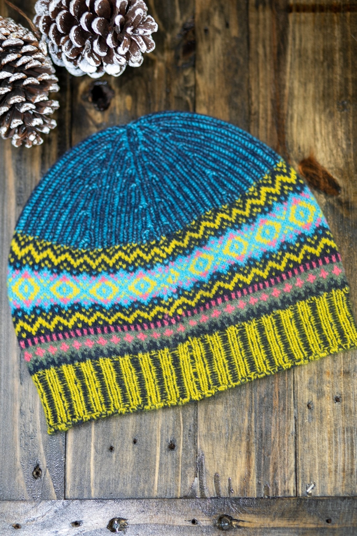 Northern Isles Merino Wool Beanie in Blue on wood background with snowy pinecone in top left - L'Atelier Global