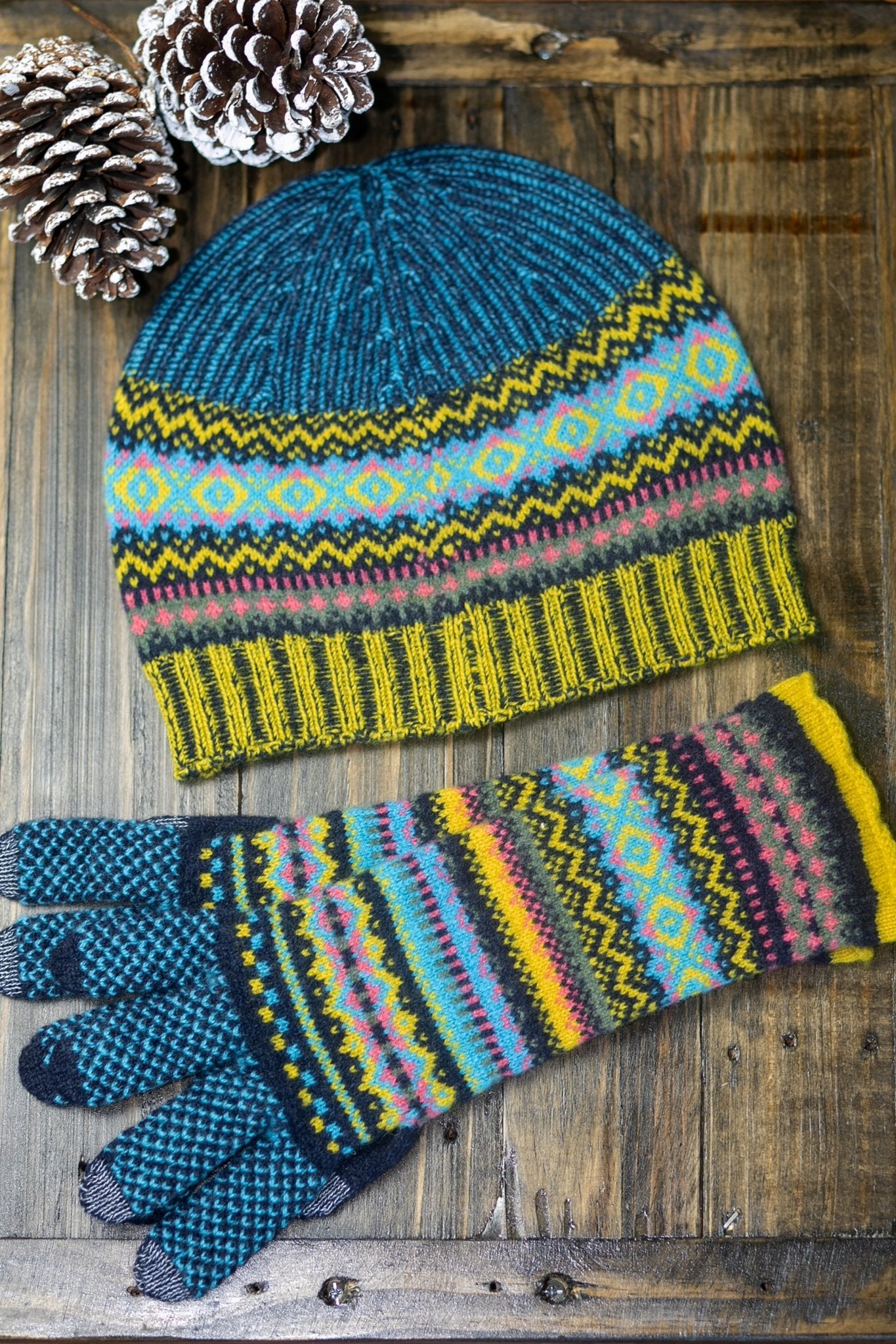Northern Isles Merino Wool Beanie and Gloves in Blue on wood background with snowy pinecone in top left - L'Atelier Global