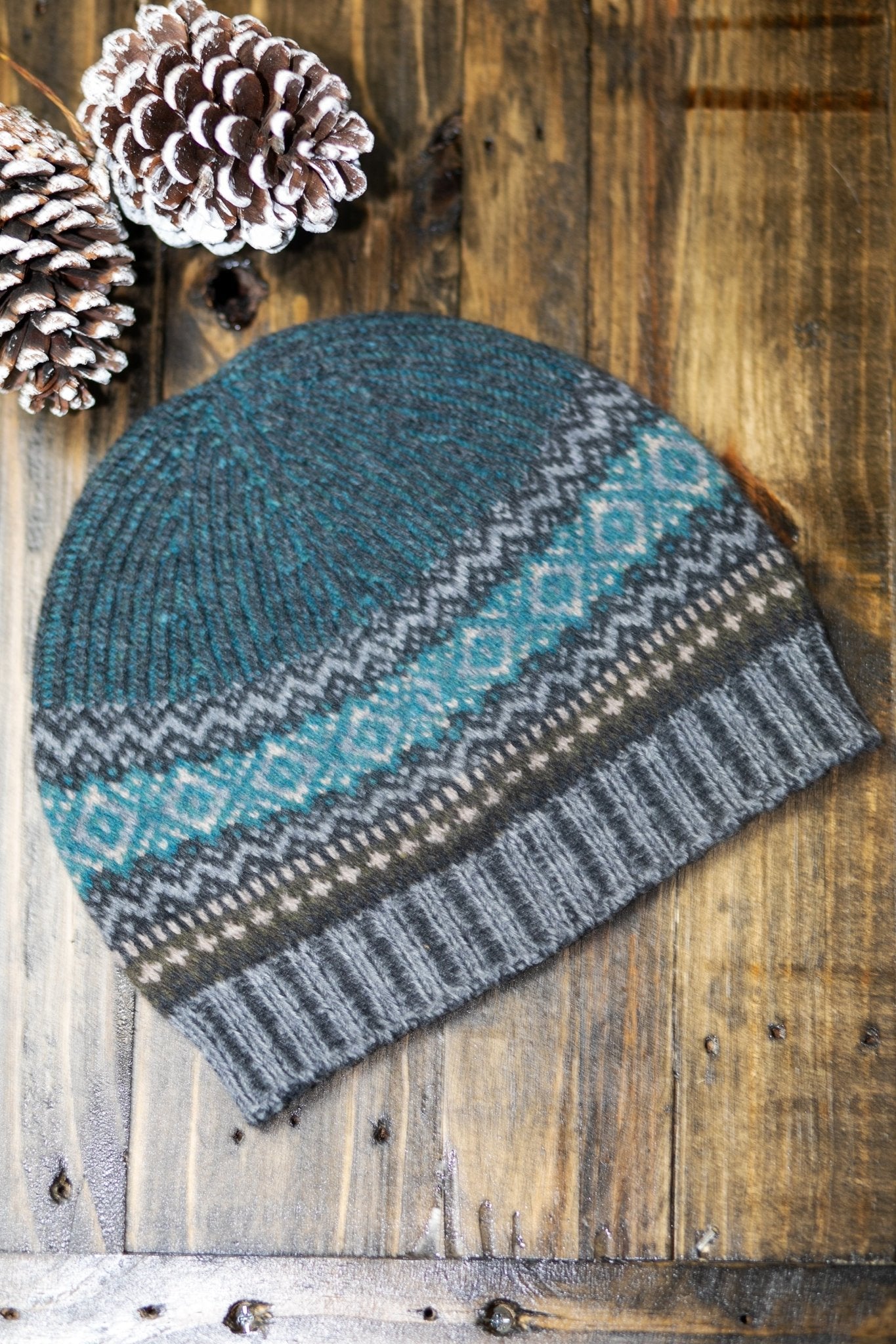 Northern Isles Merino Wool Beanie in Gray on a wood background with snowy pinecone in the top left - L'Atelier Global