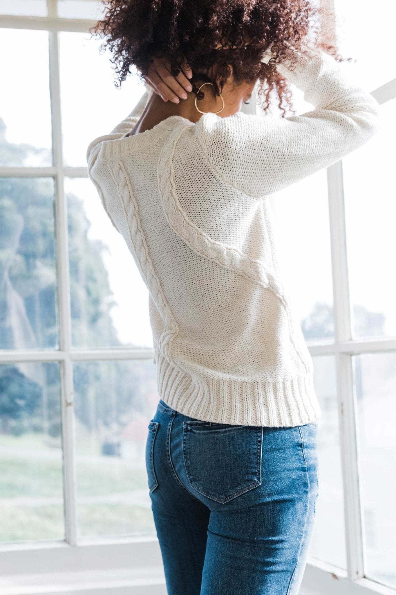 Pima Cotton Luxe Cable Sweater in white on model wearing jeans and standing showing back knitted design - L'Atelier Global