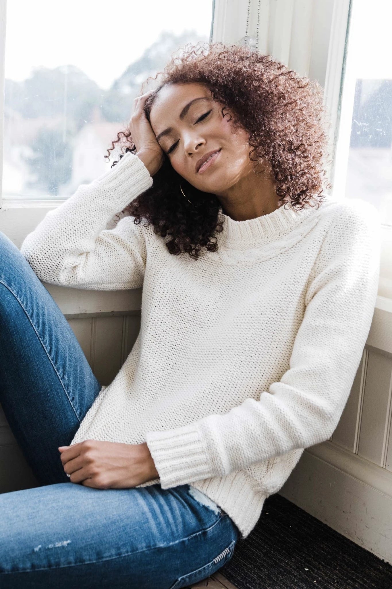 Pima Cotton Luxe Cable Sweater in white on model wearing blue jeans and sitting on couch - L'Atelier Global