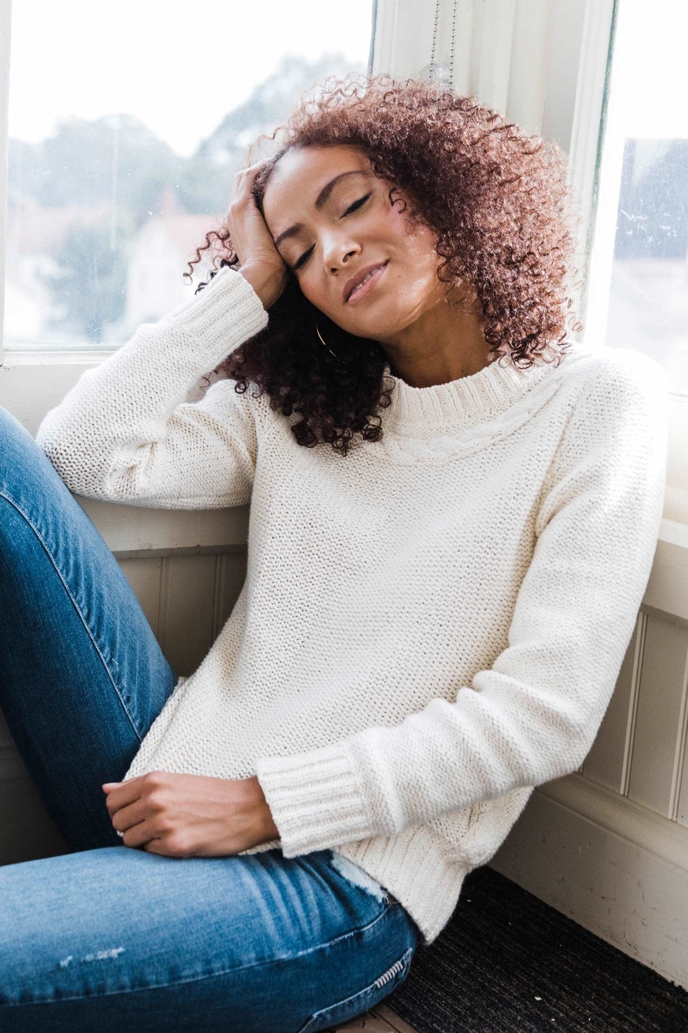 Pima Cotton Luxe Cable Sweater in white on model wearing blue jeans and sitting on couch - L'Atelier Global