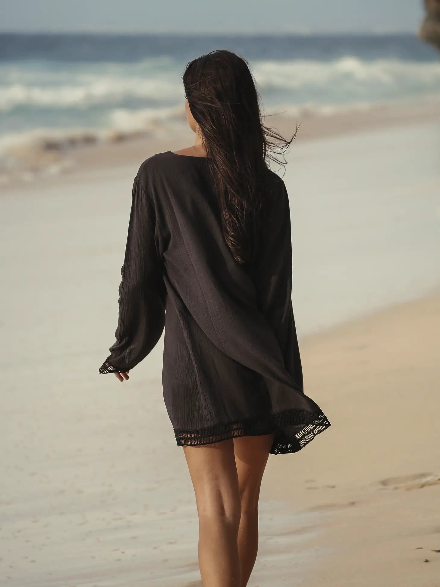 Model walking on beach wearing the Positano Turkish Cotton Cover Up Dress in Black showing back of garment.