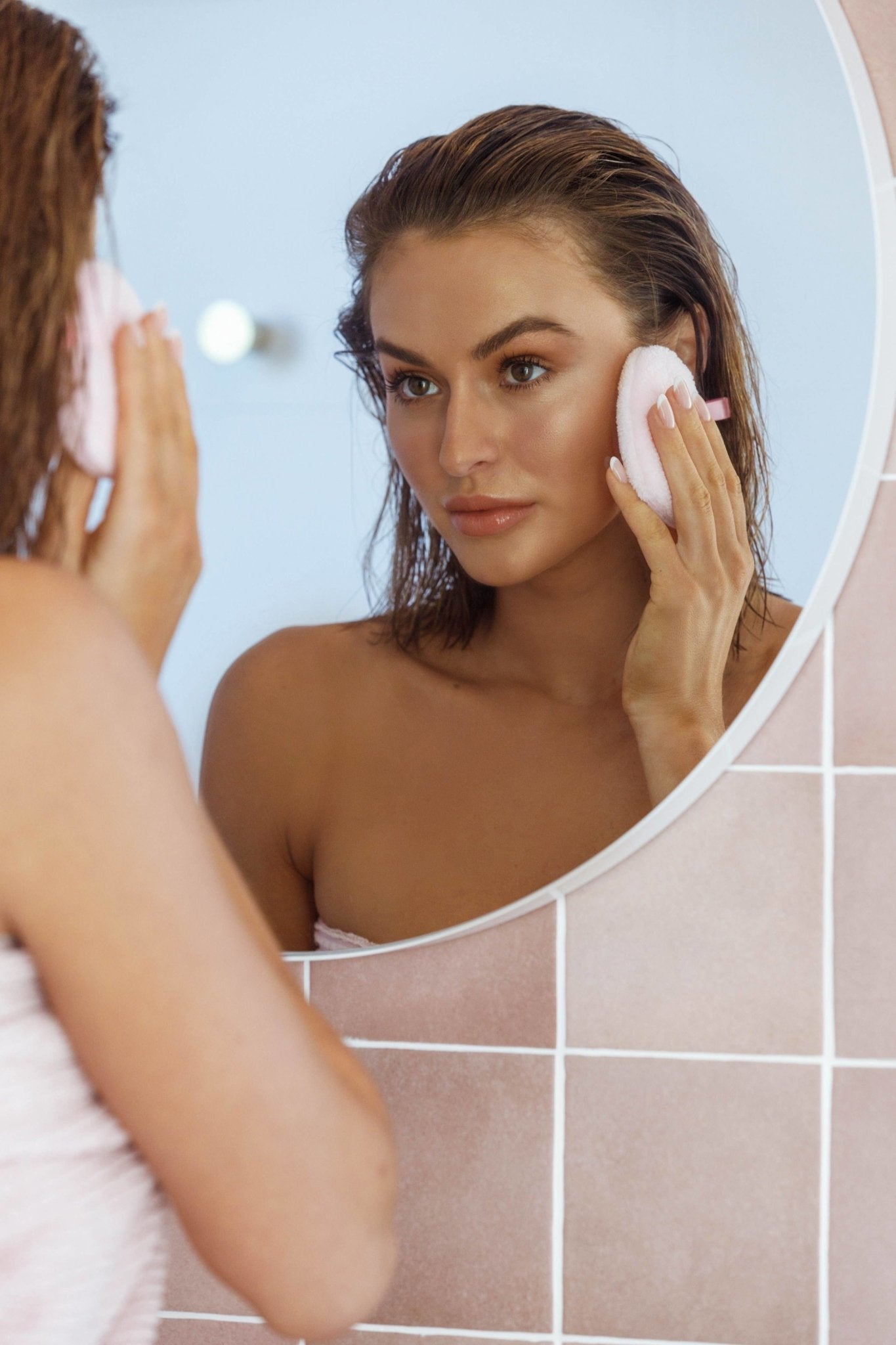 A woman is looking in the mirror holding Pure Hearts Makeup Removal Pad