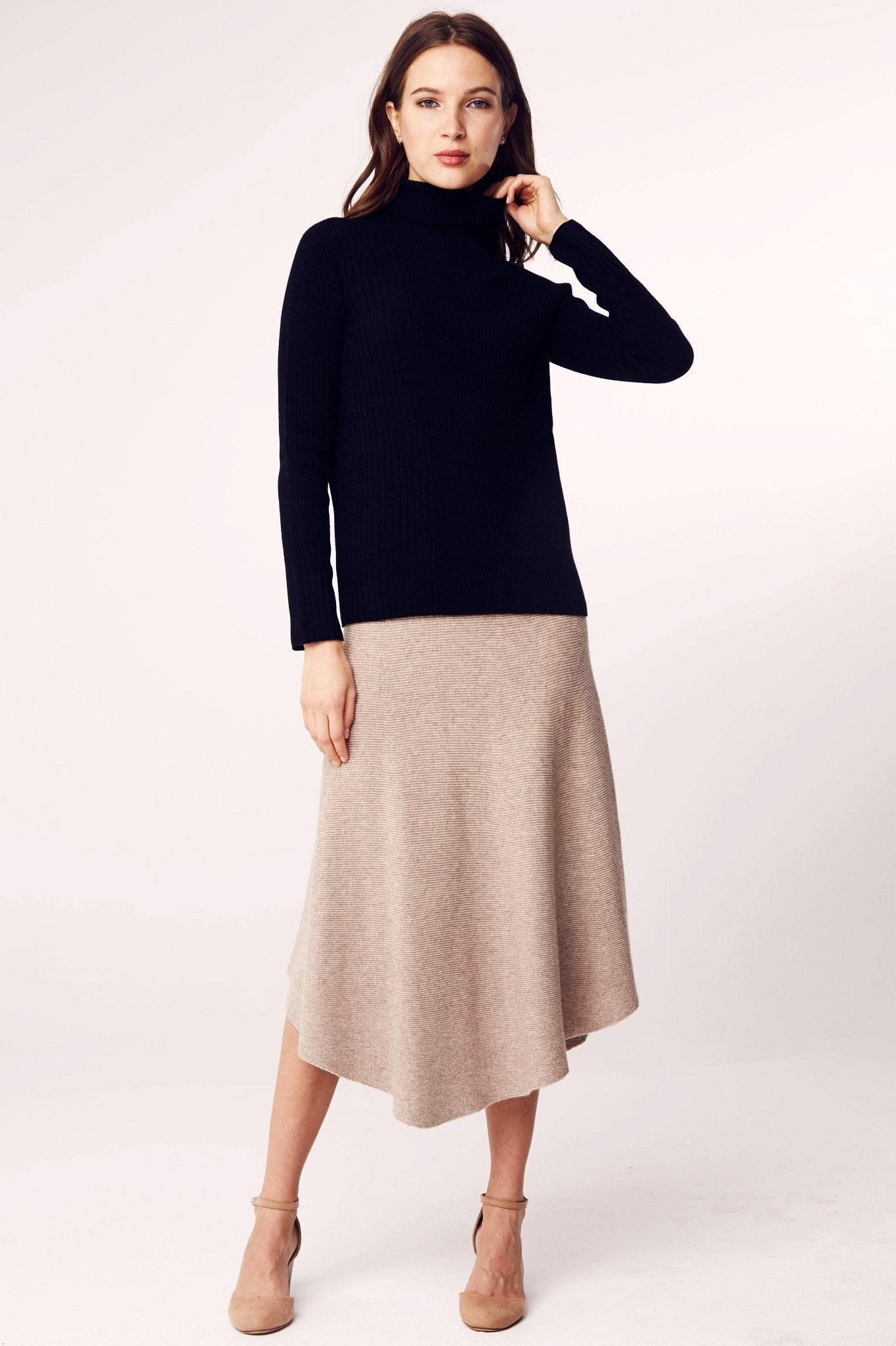 Model is standing and wearing the Seamless Ribbed Classic Turtleneck Sweater in Black on a khaki mid length skirt