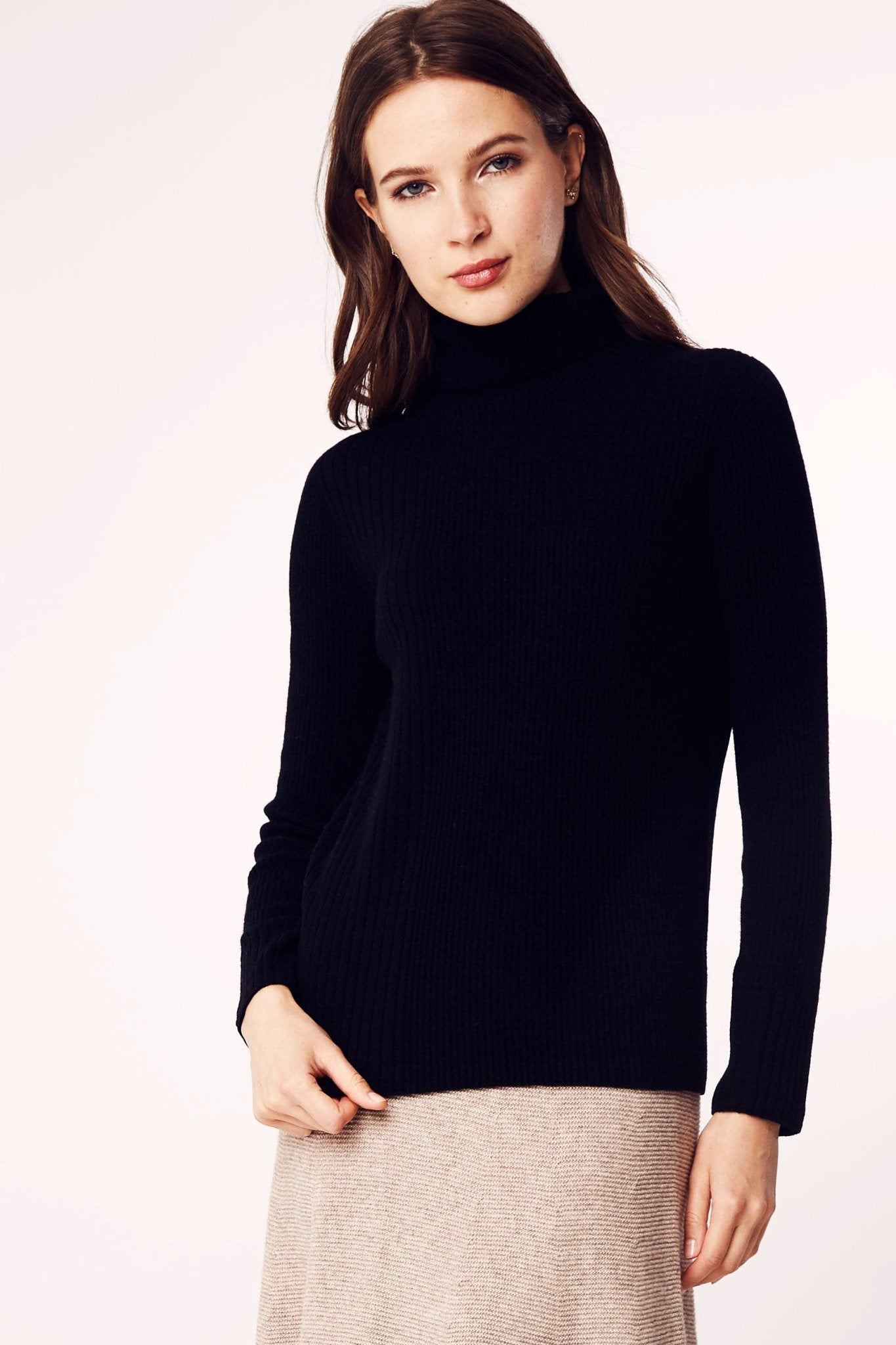 Model is standing and wearing the Seamless Ribbed Classic Turtleneck Sweater in Black on a khaki mid length skirt