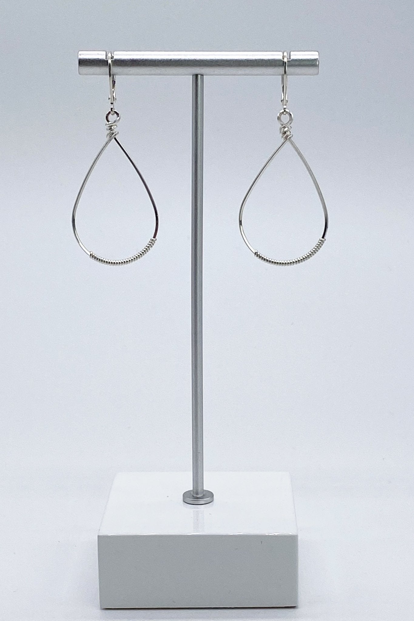 Signature Silver Small Oval Wrapped Hoops on a silver jewelry stand
