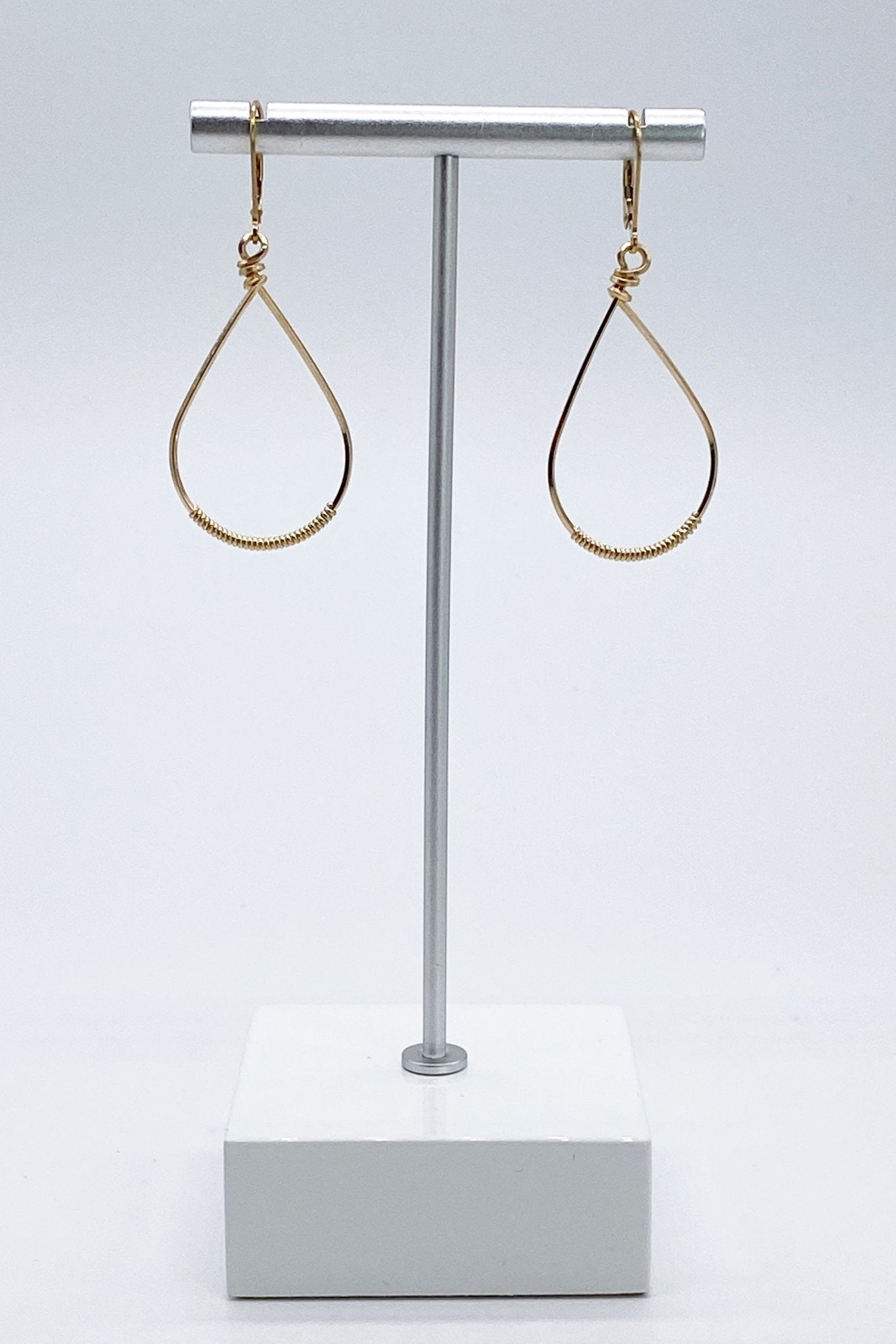 Signature Gold Small Oval Wrapped Hoops on a silver jewelry stand