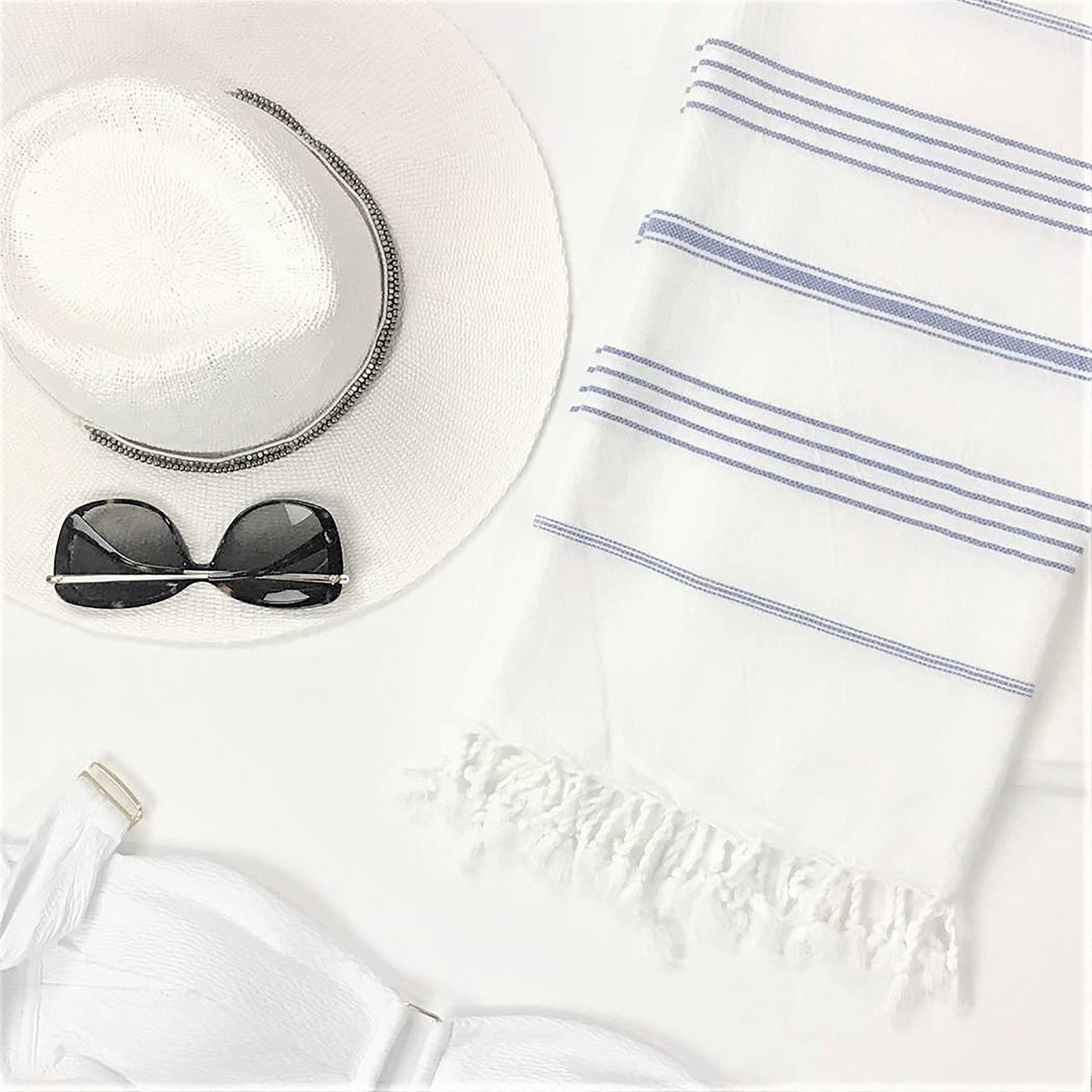 Signature Turkish Cotton Striped Towel in Pink on a white background with a straw sun hat, white bikini strapless top and sunglasses.