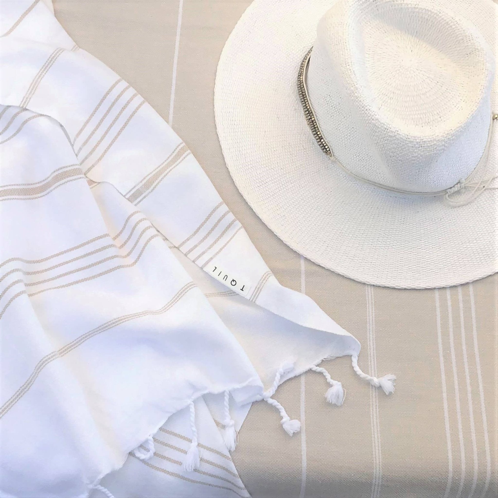 Signature Turkish Cotton Striped Towel in Tan on a tan lounging chair background with a straw sun hat