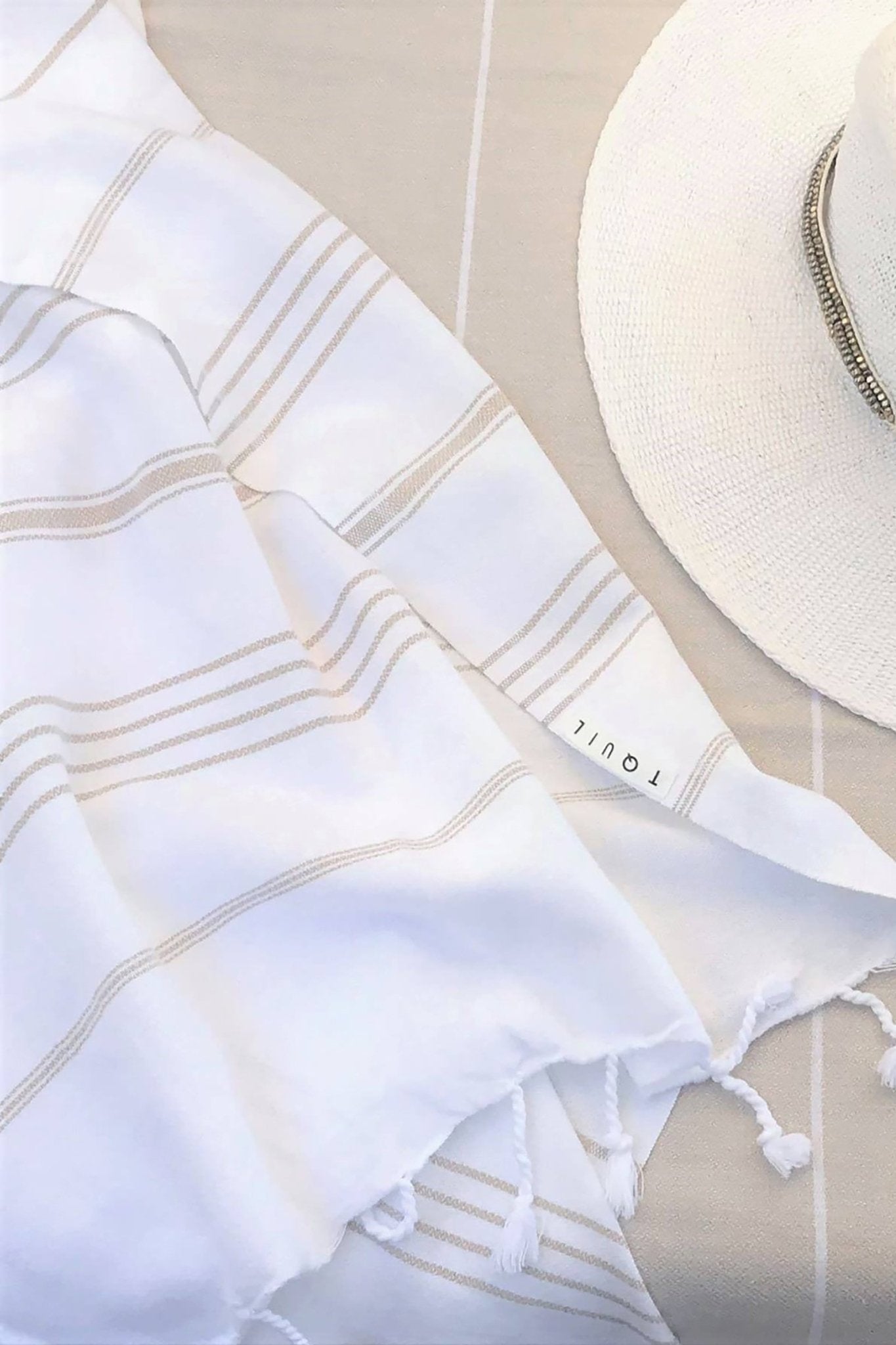 Signature Turkish Cotton Striped Towel in Tan on a tan lounging chair background with a straw sun hat