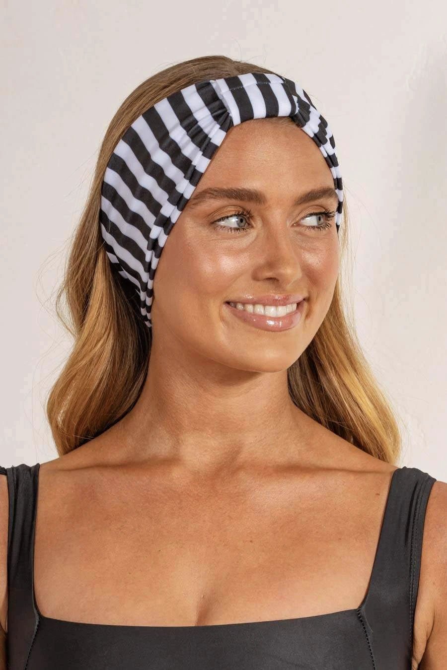 A smiling person wearing a black and white striped headband designed to sweep hair off the face.