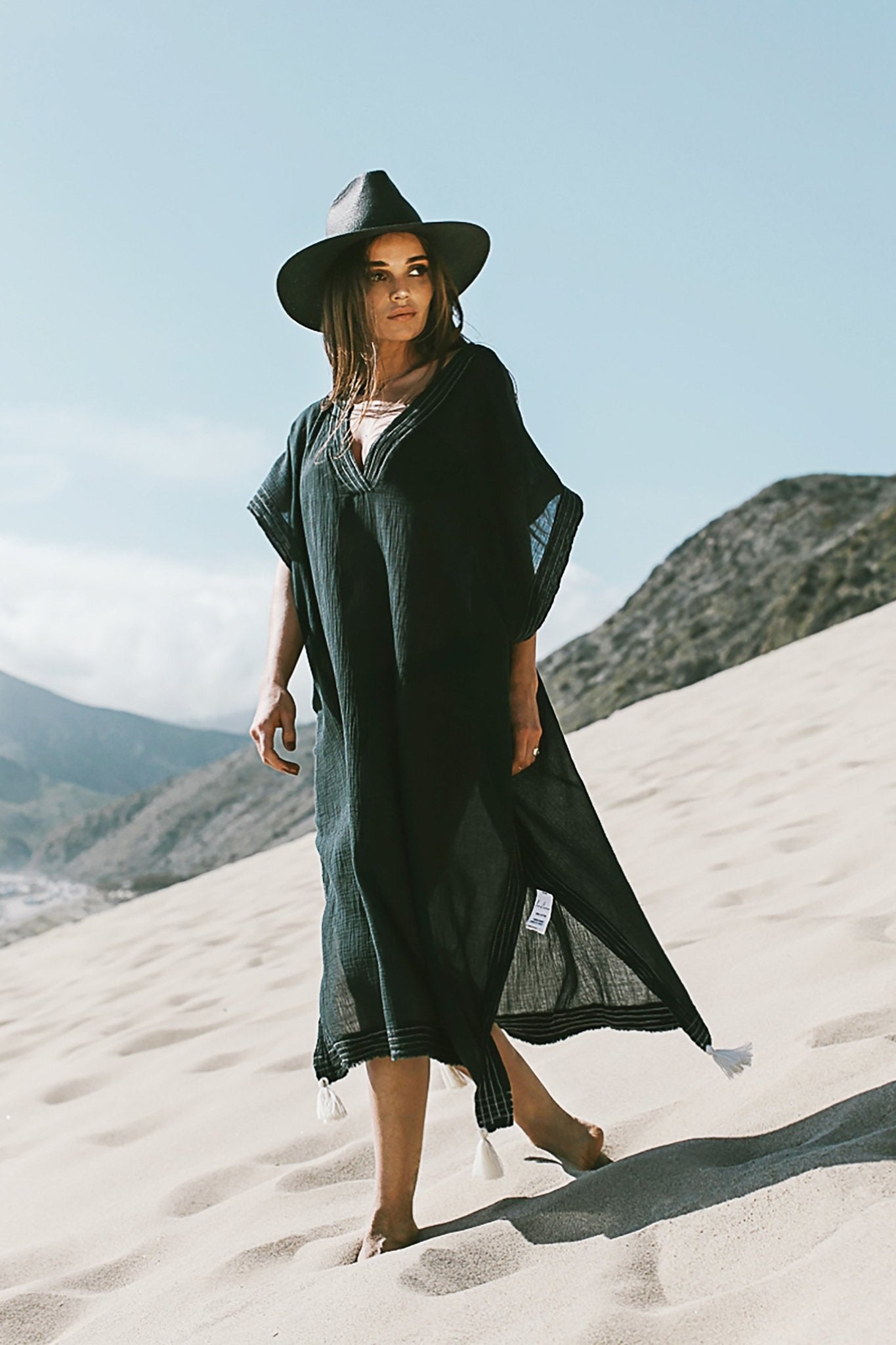 Summer Ready Breezy Kaftan in Black on a woman walking on beach wearing a black hat.