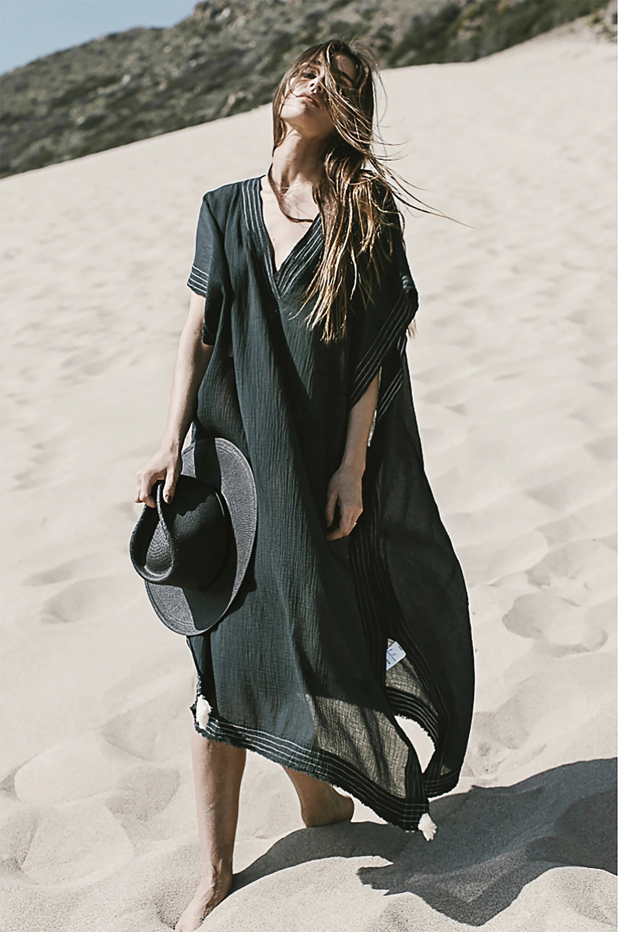 Woman wearing the Summer Ready Breezy Kaftan in Black on beach holding a black hat