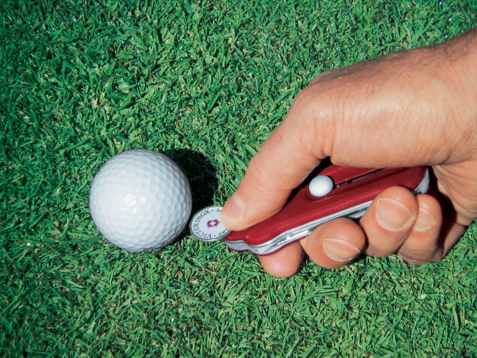 Swiss Golf Tool shown in use on a putting green, the ball marker is placed on the green by the golf ball.