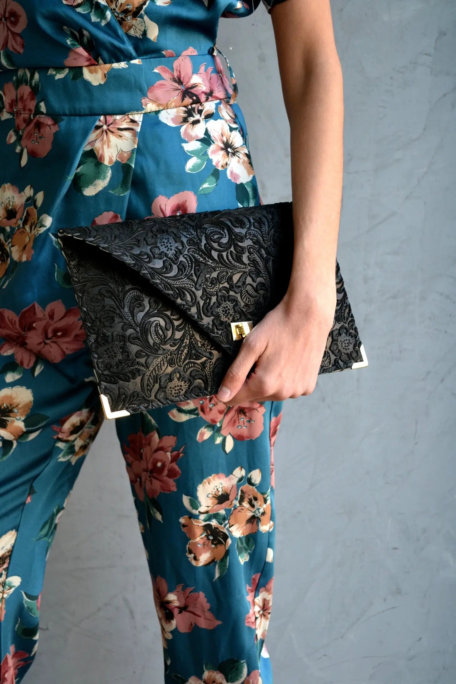 A model in a floral pantsuit holding the Symmetria Floral All Day Leather Clutch