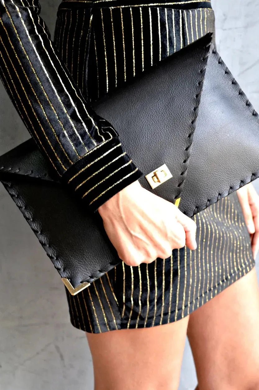 Symmetria Leather All Day Clutch in black held by a model in gold black striped dress