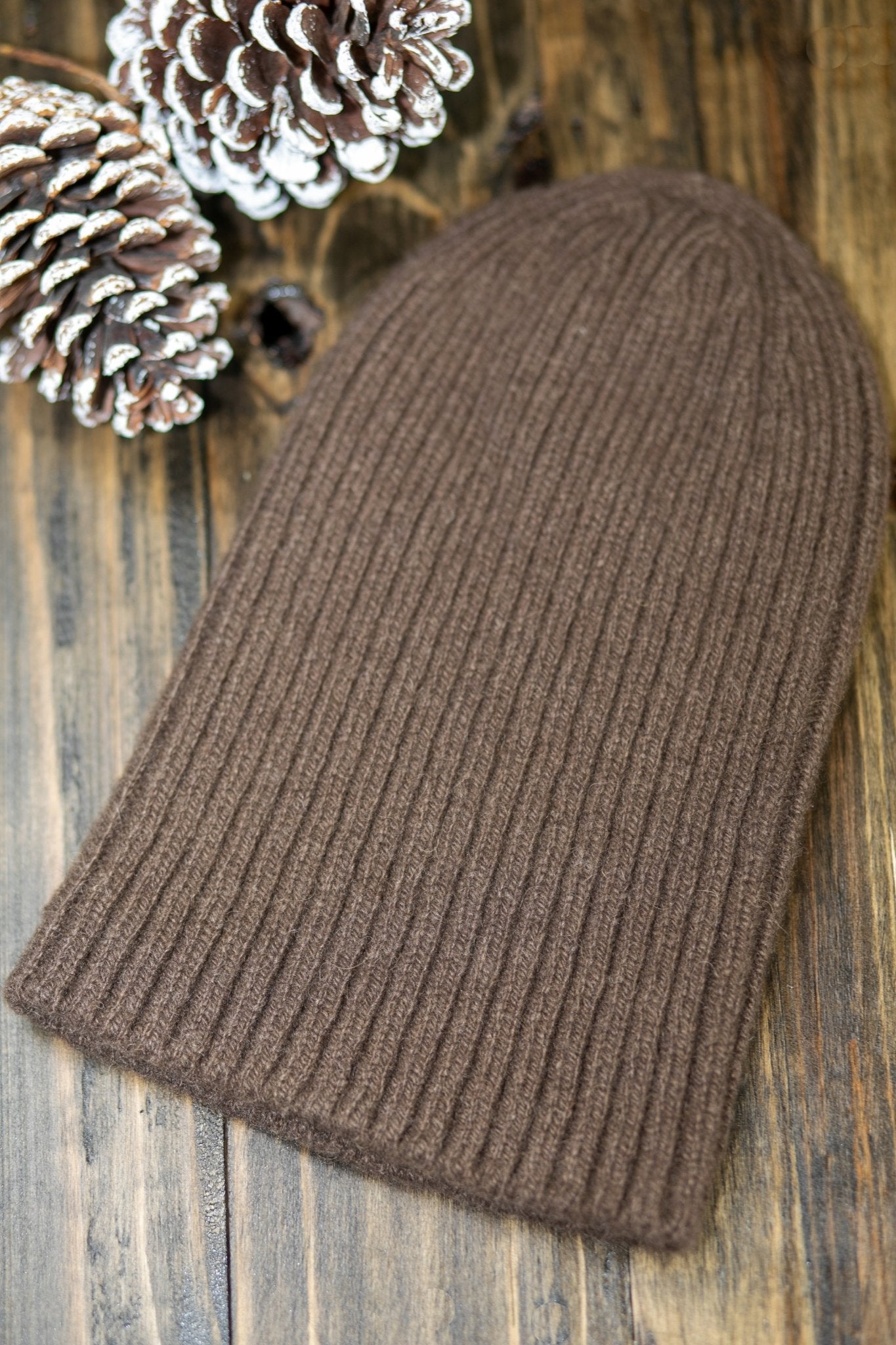 The American Bison Wool Beanie laying on a wooden table with a snowy pinecone on the top left corner - L'Atelier Global