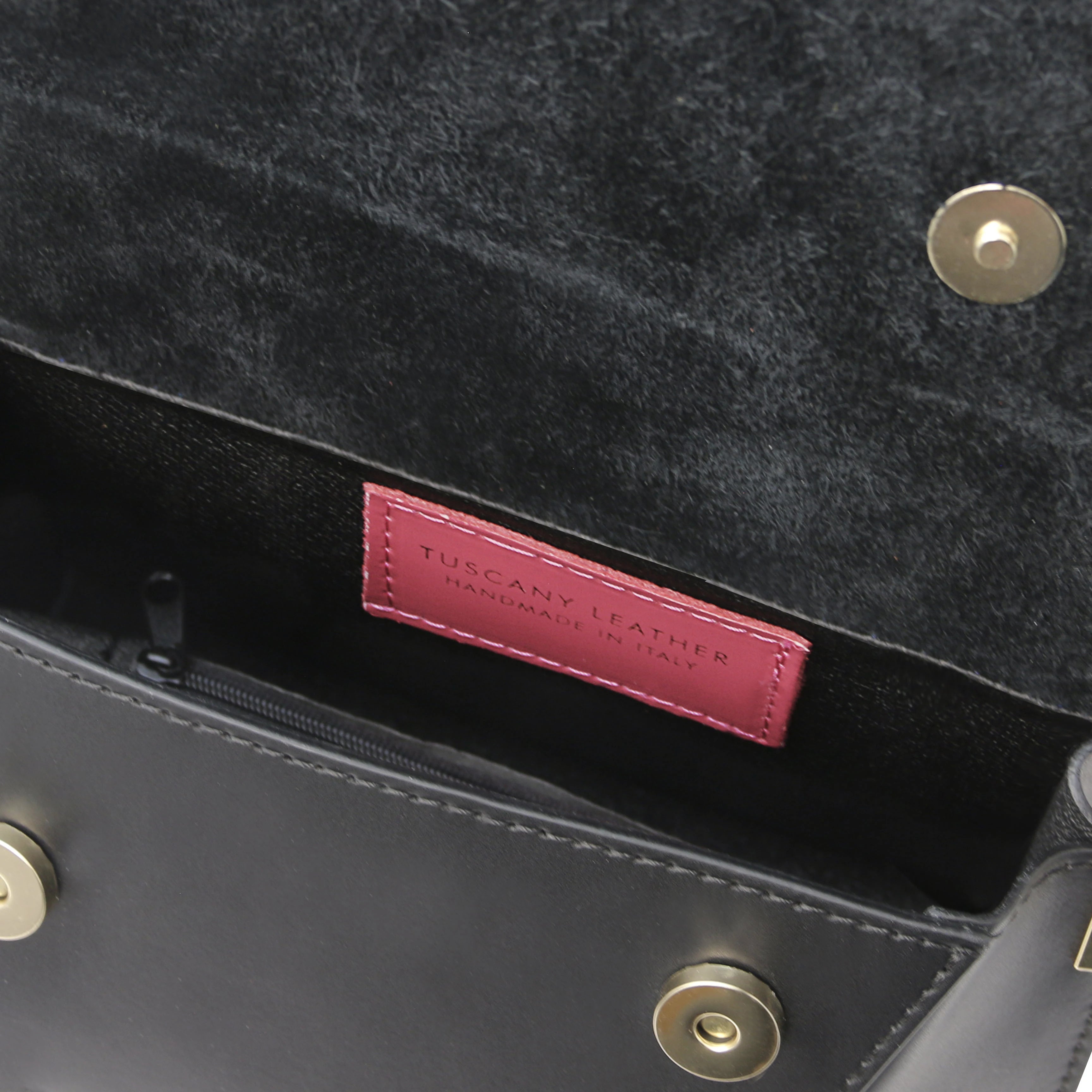 Interior zip pocket view TL Leather Assymetrical Shoulder Bag in Black showing magnetic button closures and Tuscany Leather branding