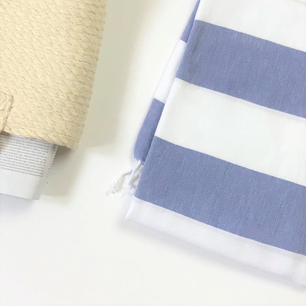 Turkish Aegean Cotton Cabana Towel in blue and white stripes laying on the beach