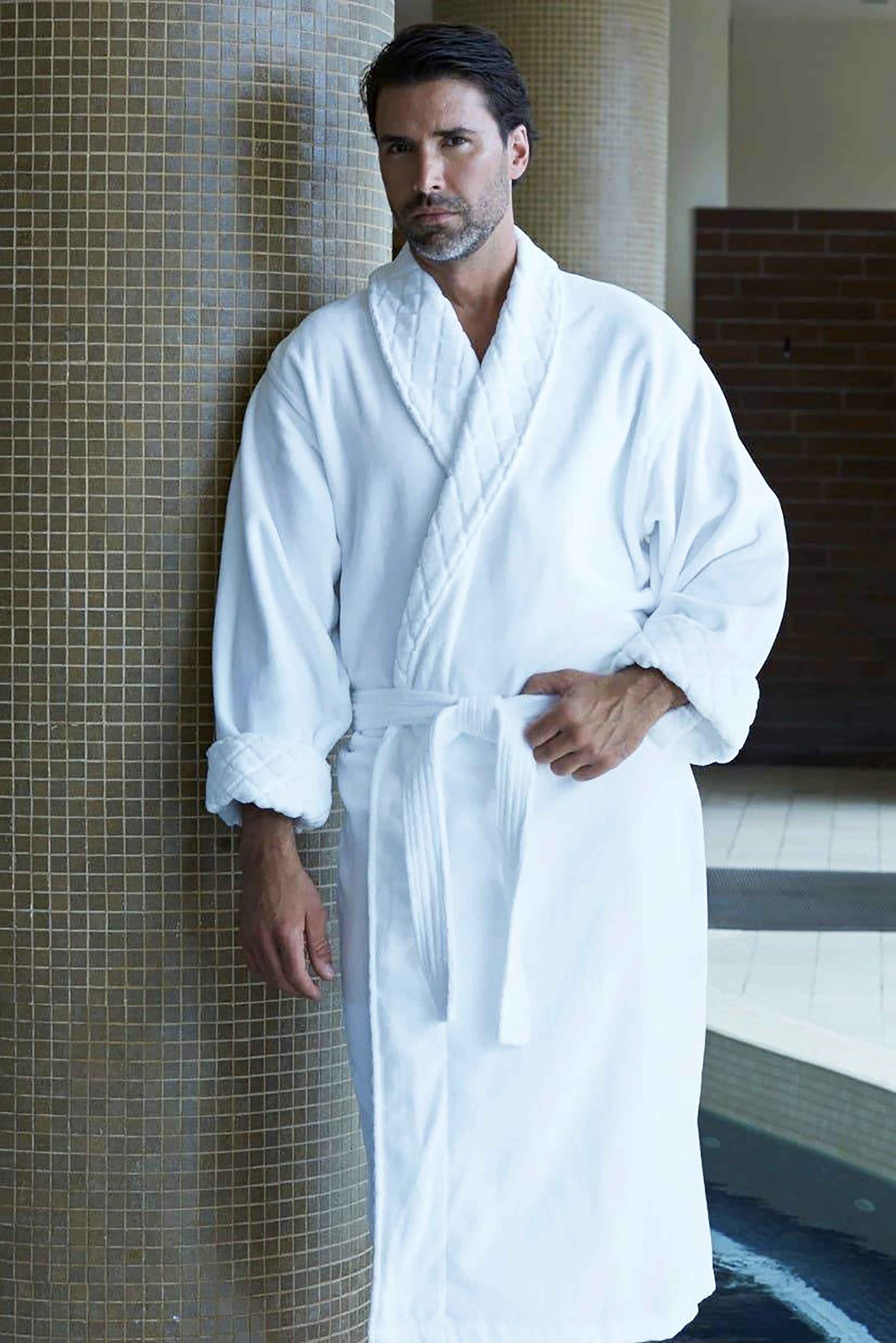 A male model is wearing the Unisex Luxe Jacquard Cotton Terry Velour Robe in a bathroom setting - L'Atelier Global