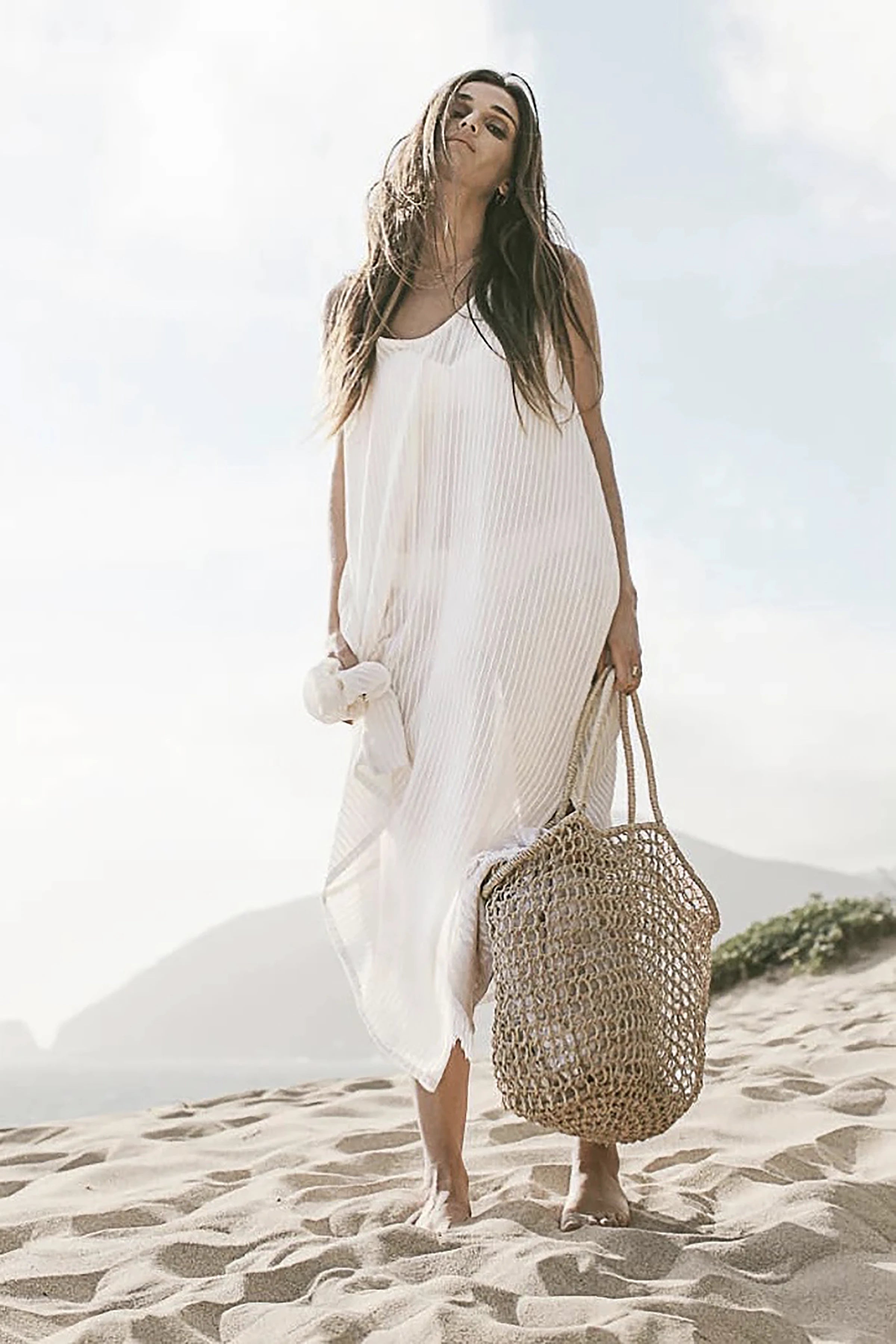 Yaz Dress in Natural White Stripes on model holding a natural crochet tote bag on the beach.