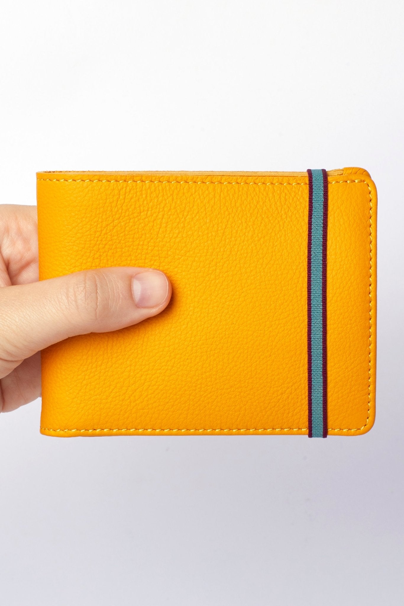 A man's hand holding Yellow Minimalist Wallet With Coin Pocket with elastic closure on white background - L'Atelier Global
